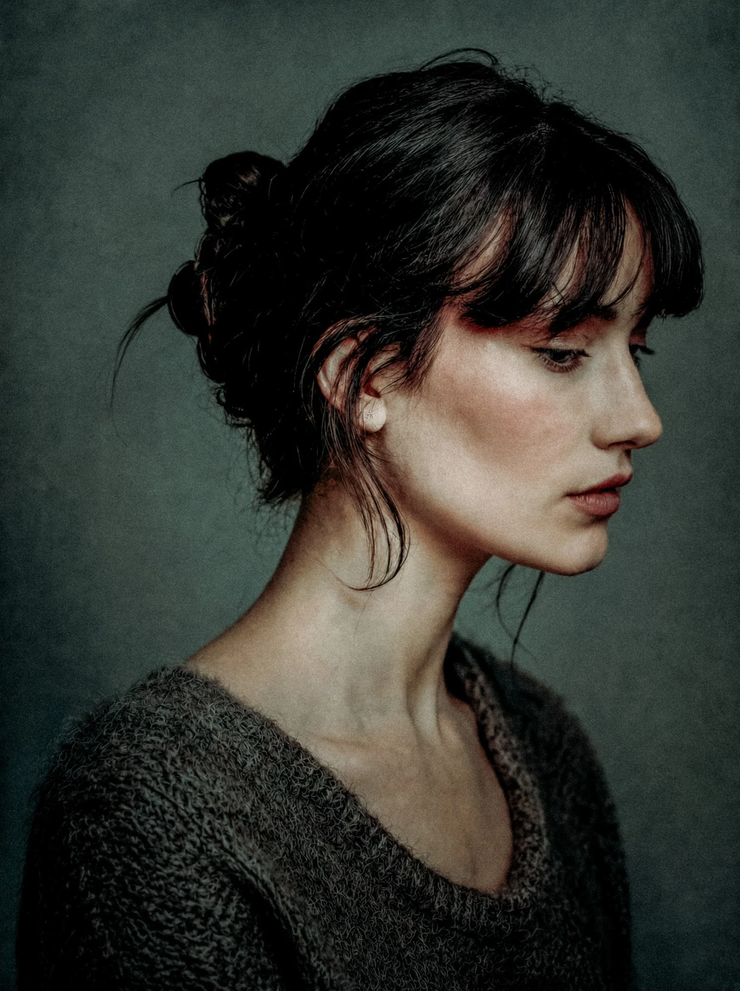 A portrait of a woman with dark hair in an elegant, high-collared black dress with floral embroidery, set against a warm, textured brown background.