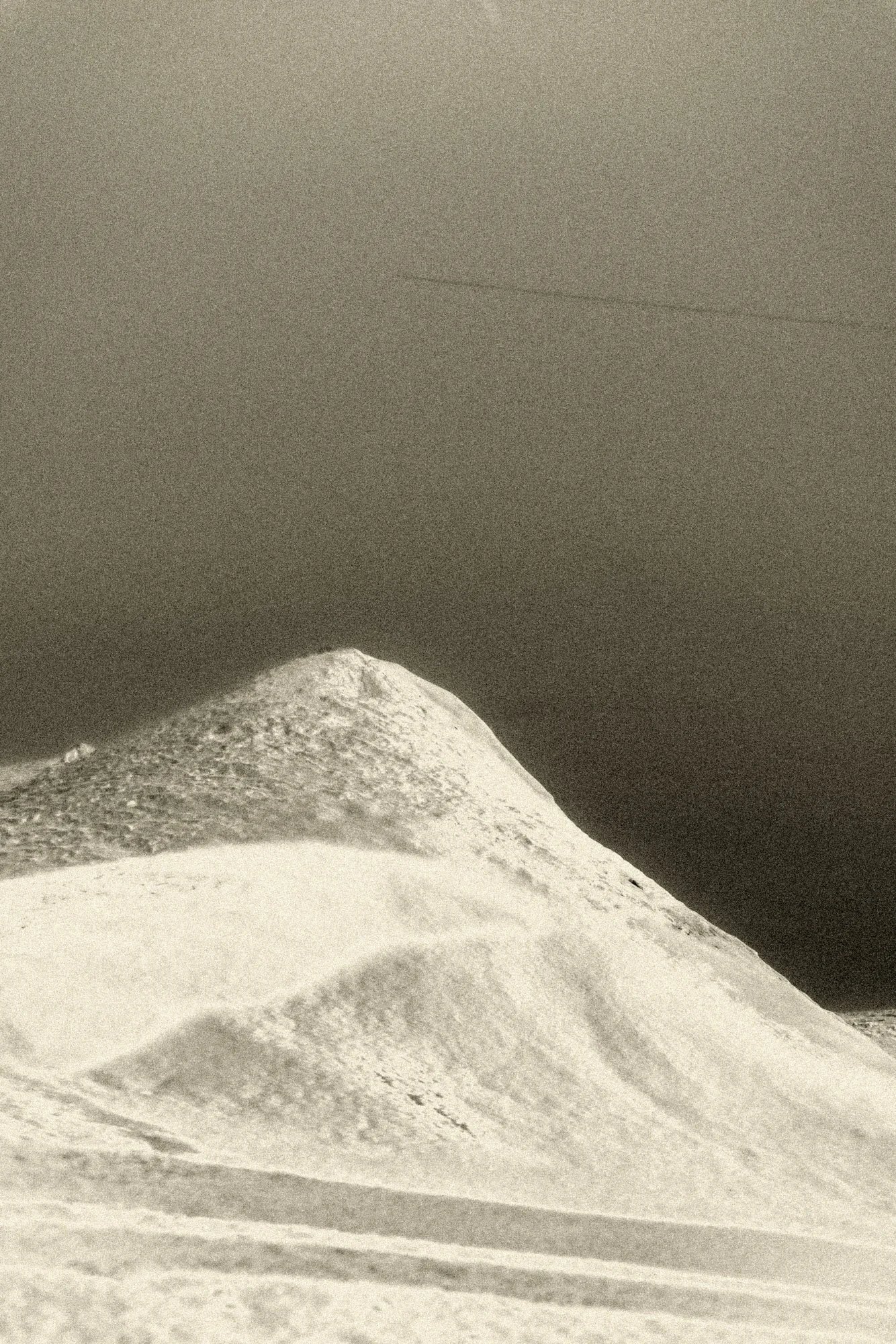 High-contrast black-and-white landscape of a bright snow peak rising into an open sky, a minimalist mountain photograph conveying scale and stillness.