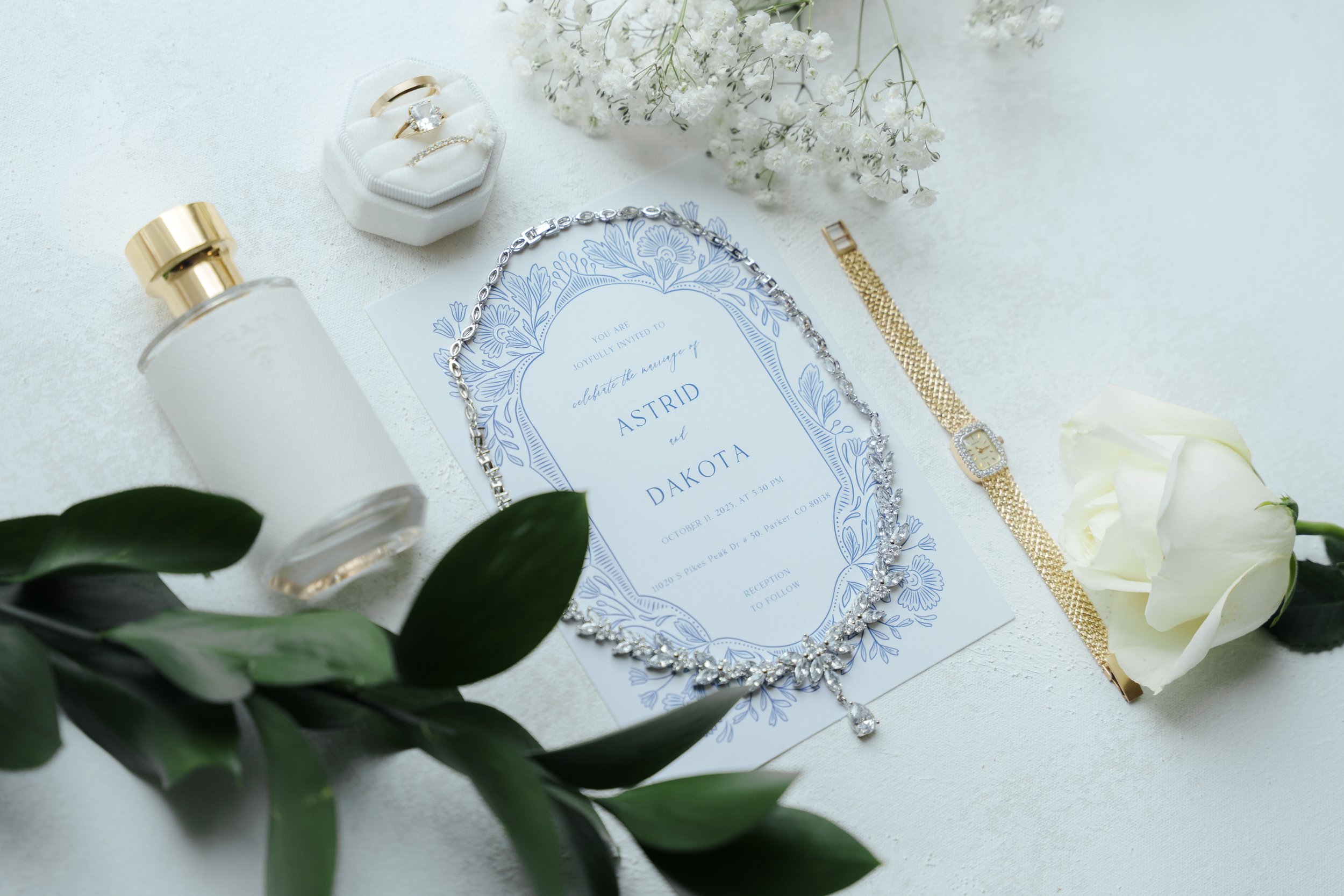 Wedding invitation with jewelry, flowers, and accessories arranged on a white surface.