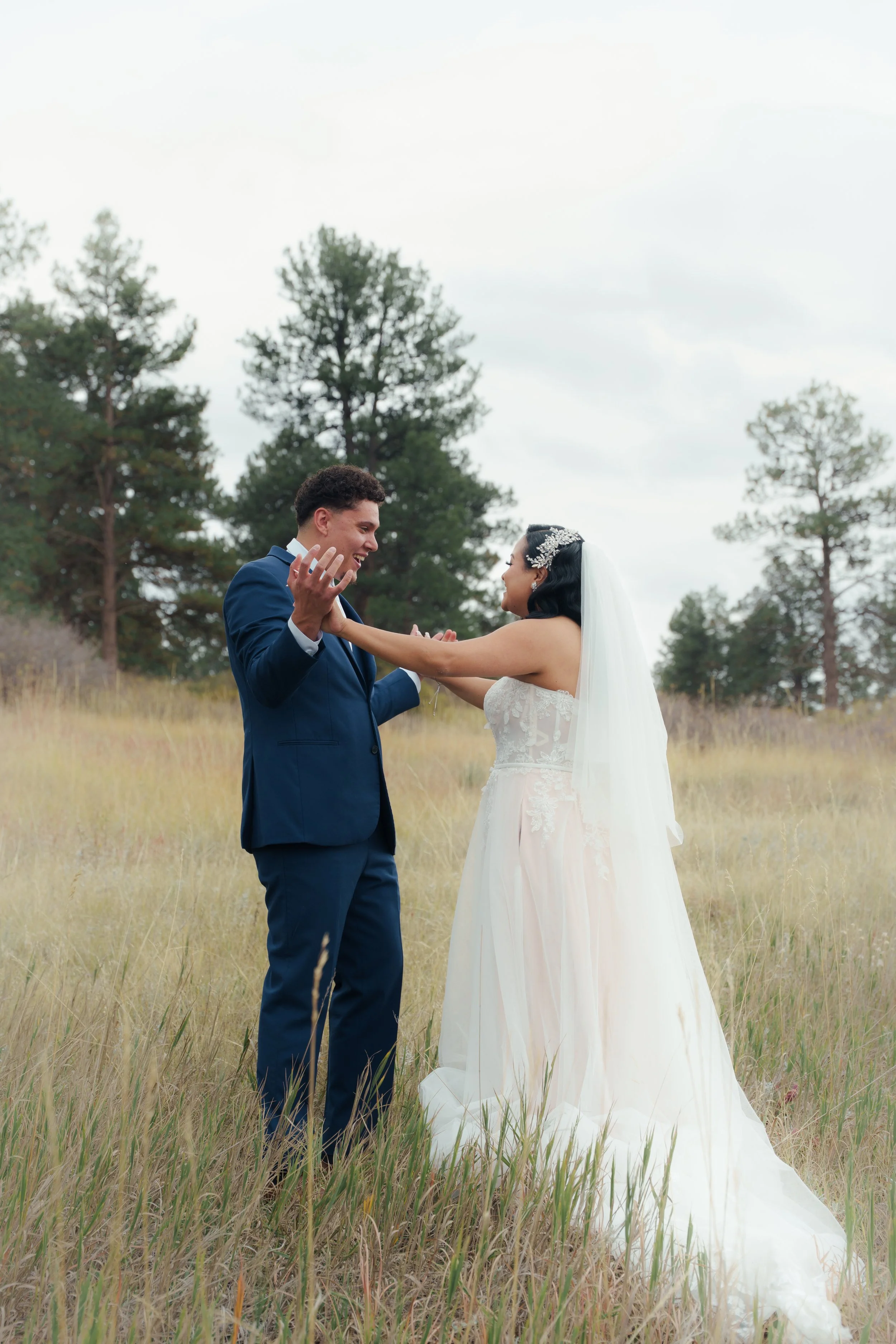 Bride and groom sharing a joyful moment outdoors in a field with trees in the background.