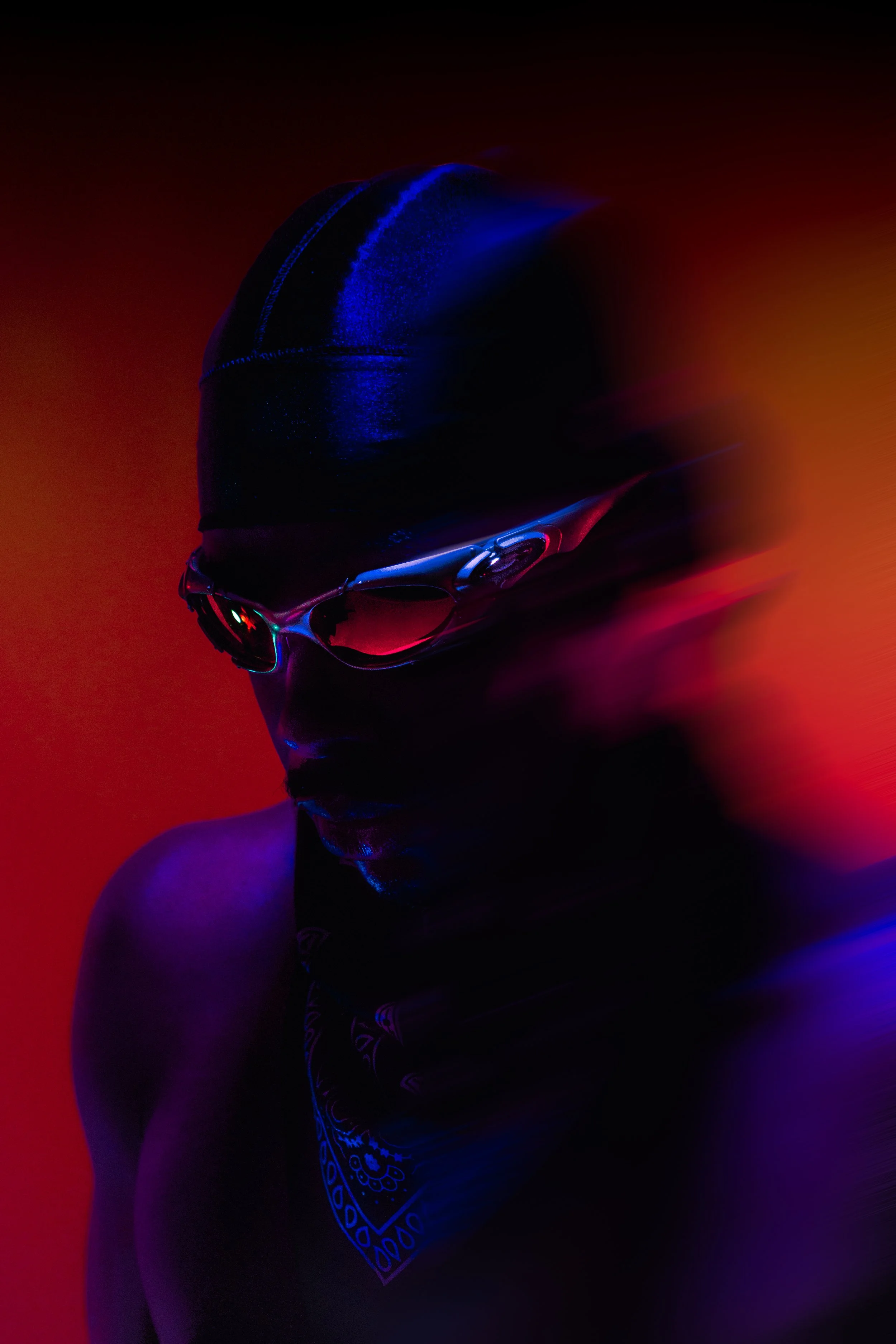 A person wearing a black swim cap, sports goggles, and a bandana, with neon lighting creating a colorful glow, against a dark background.