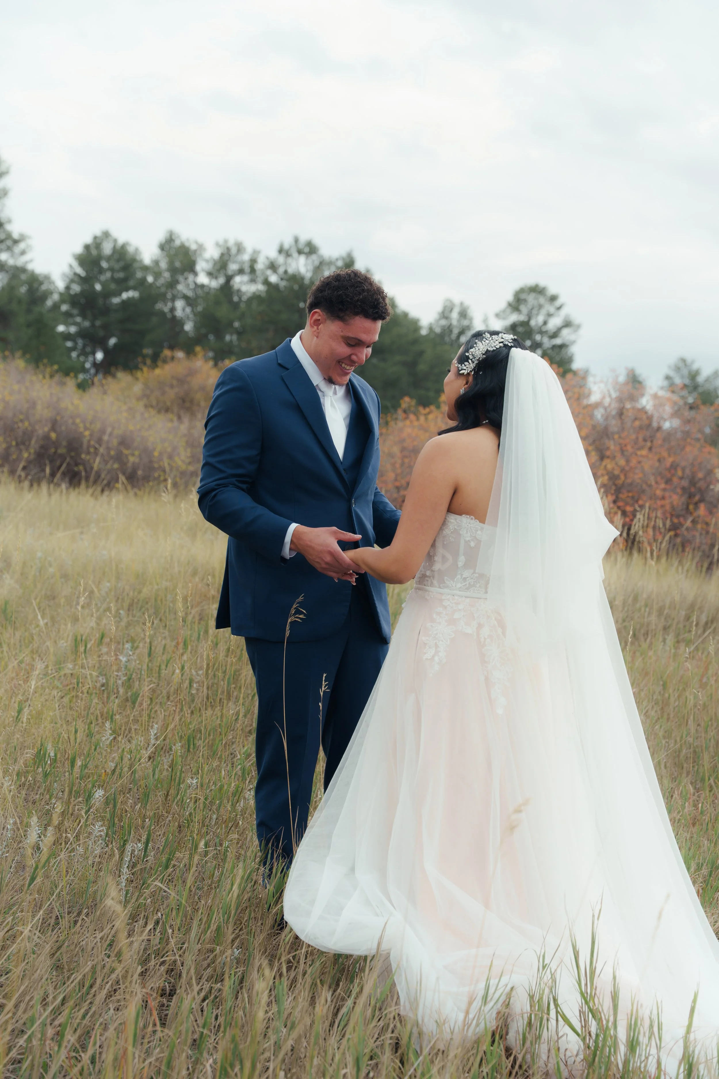 A bride and groom holding hands and smiling in a grassy field during their wedding ceremony outdoors.