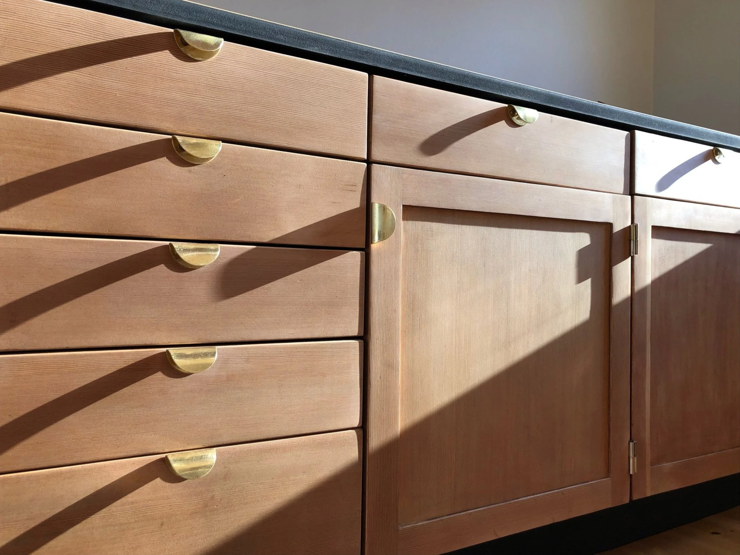 Wooden kitchen cabinets with brass cup handles and sunlight shadows