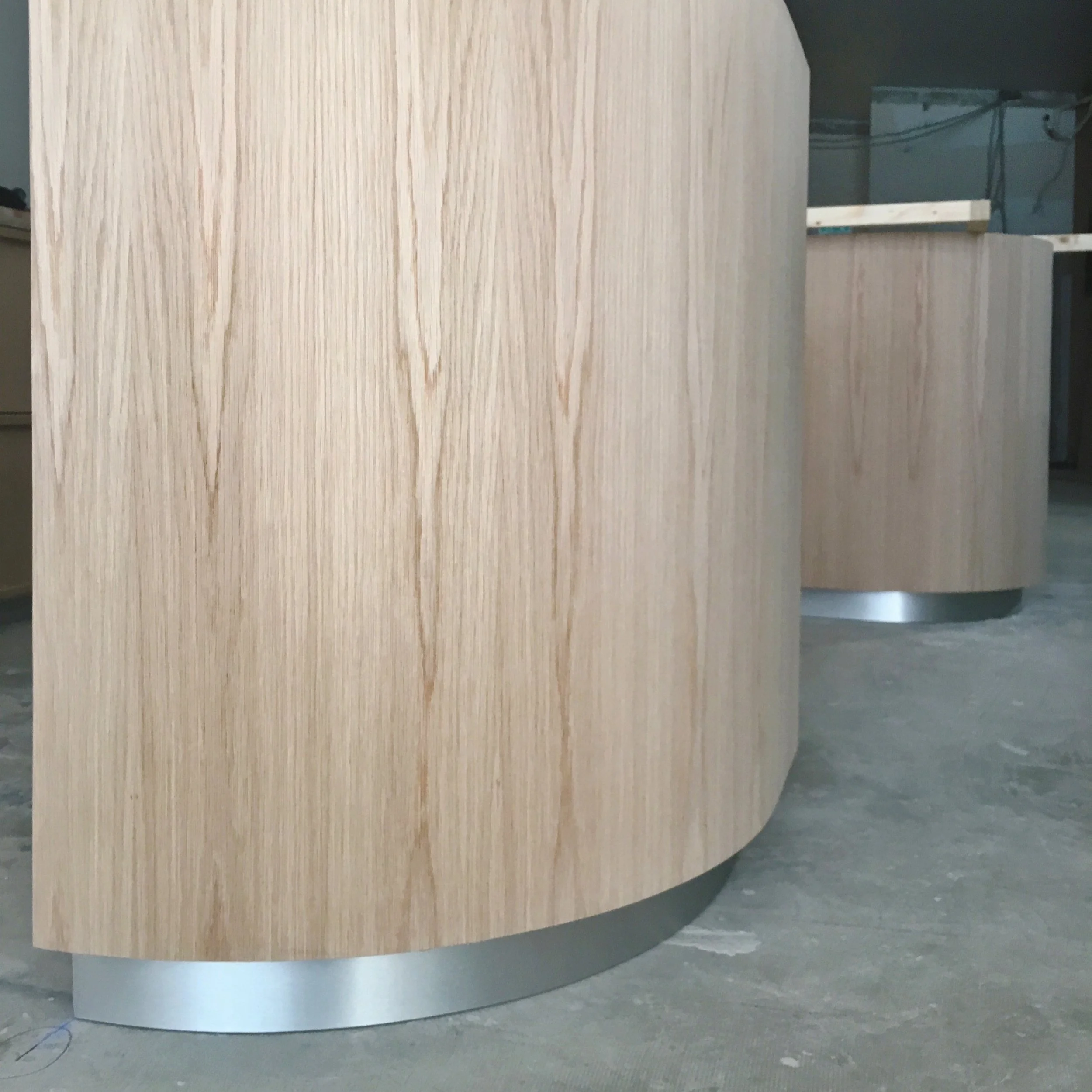 Curved wooden structures with light wood grain pattern and silver base on a concrete floor.