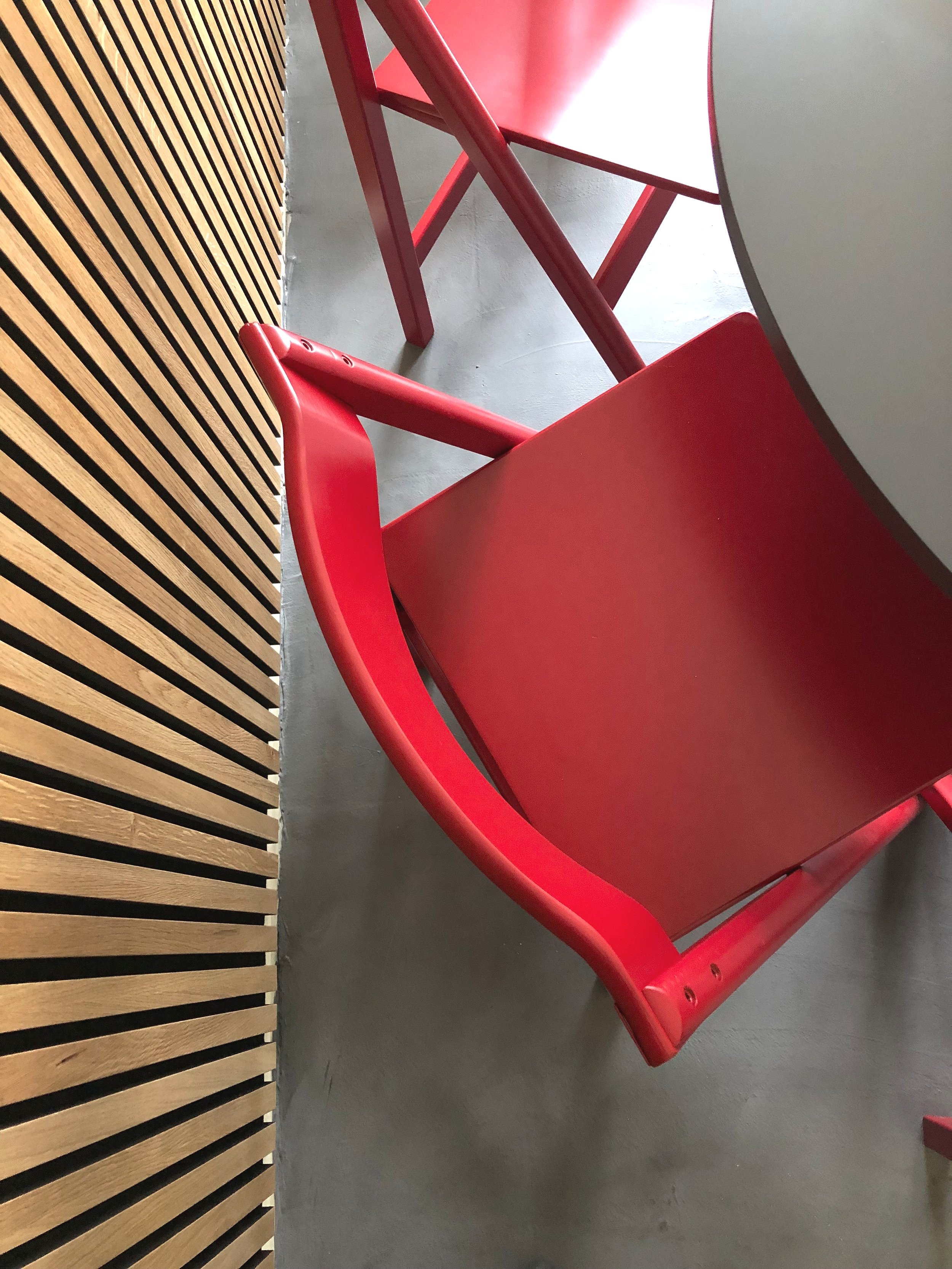 Red wooden chairs near a round gray table and slatted wooden wall