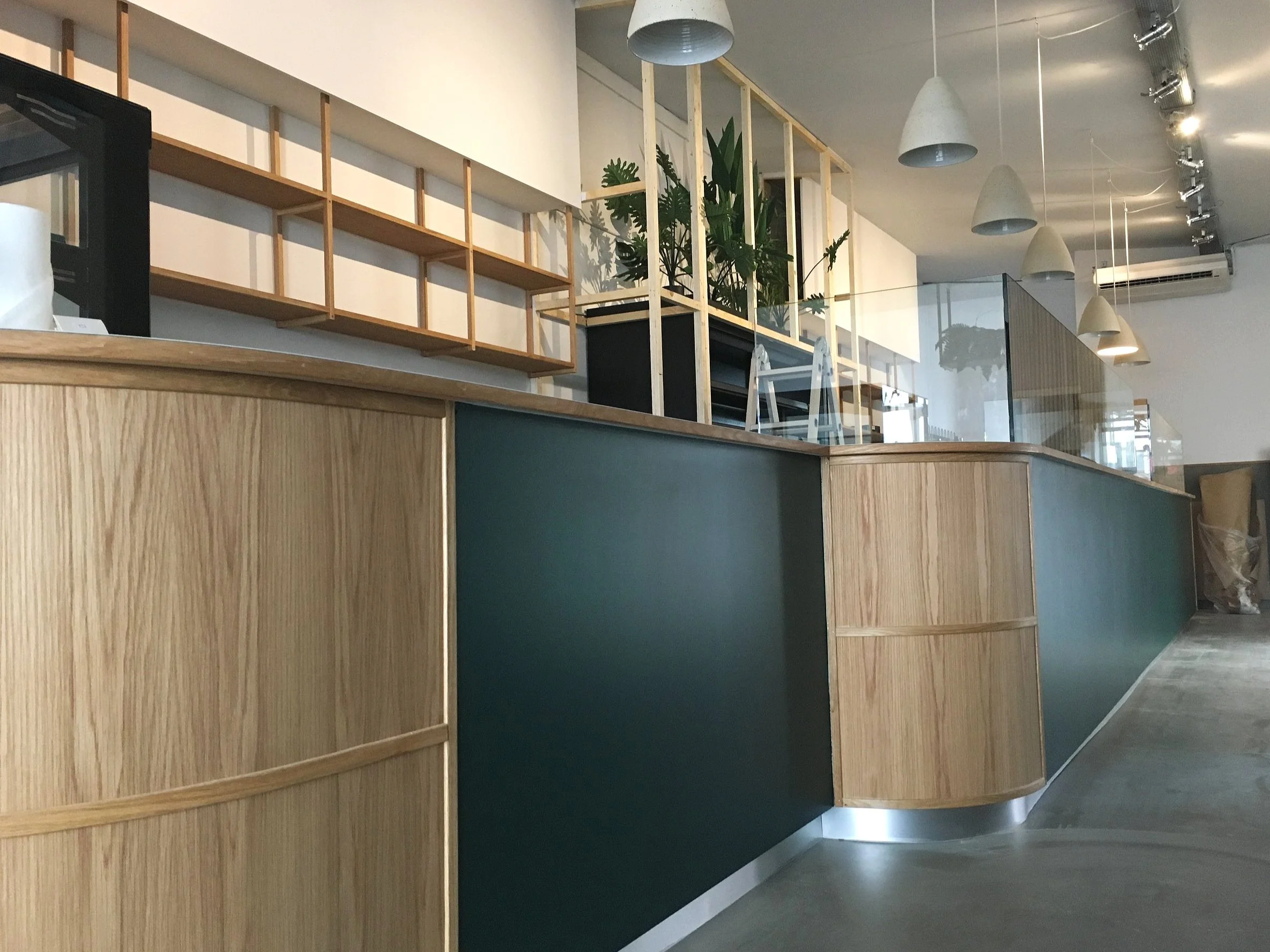 Modern café interior with a wooden counter, pendant lighting, plants, and shelving.