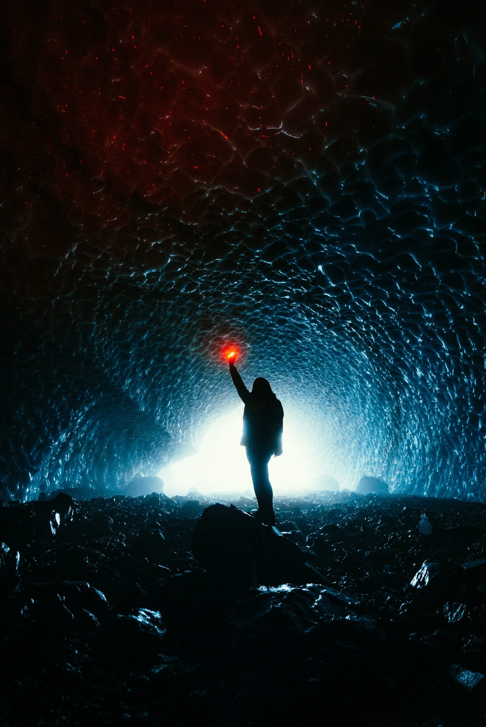 A silhouette of a person holding a red flare inside a dark, textured cave with a glowing opening in the background.