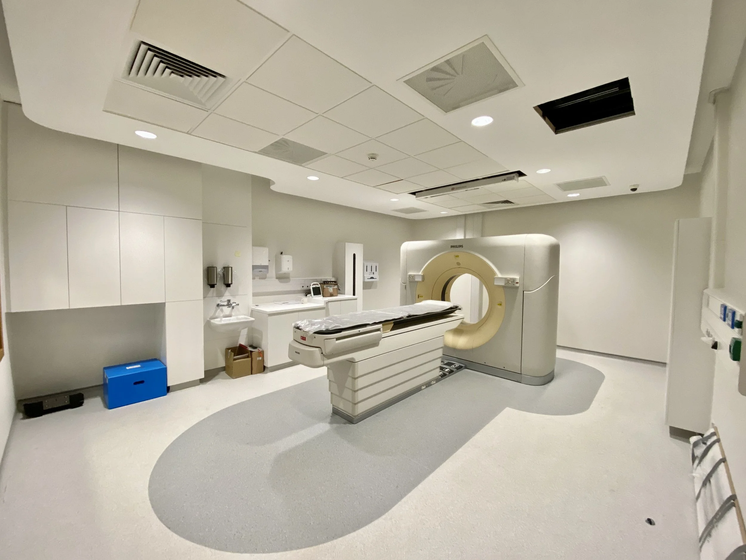 A medical imaging room with a CT scanner, white cabinetry, medical supplies, and equipment, all in a clean, sterile environment.