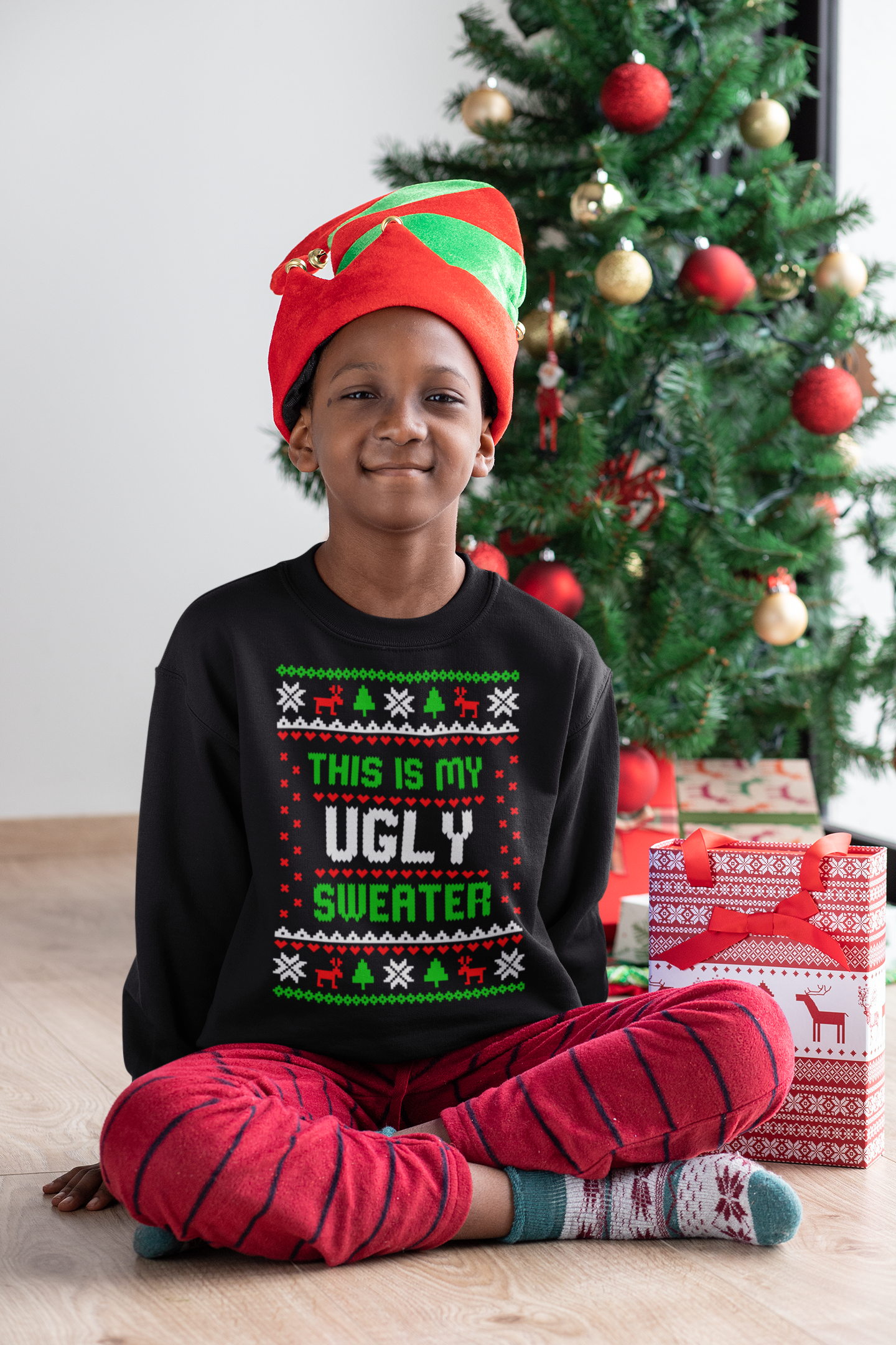 mockup-of-a-kid-with-a-crewneck-sweatshirt-sitting-next-to-a-christmas-tree-30358.png