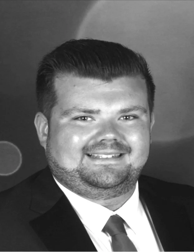Black and white portrait of a smiling man in a suit and tie, with short styled hair.