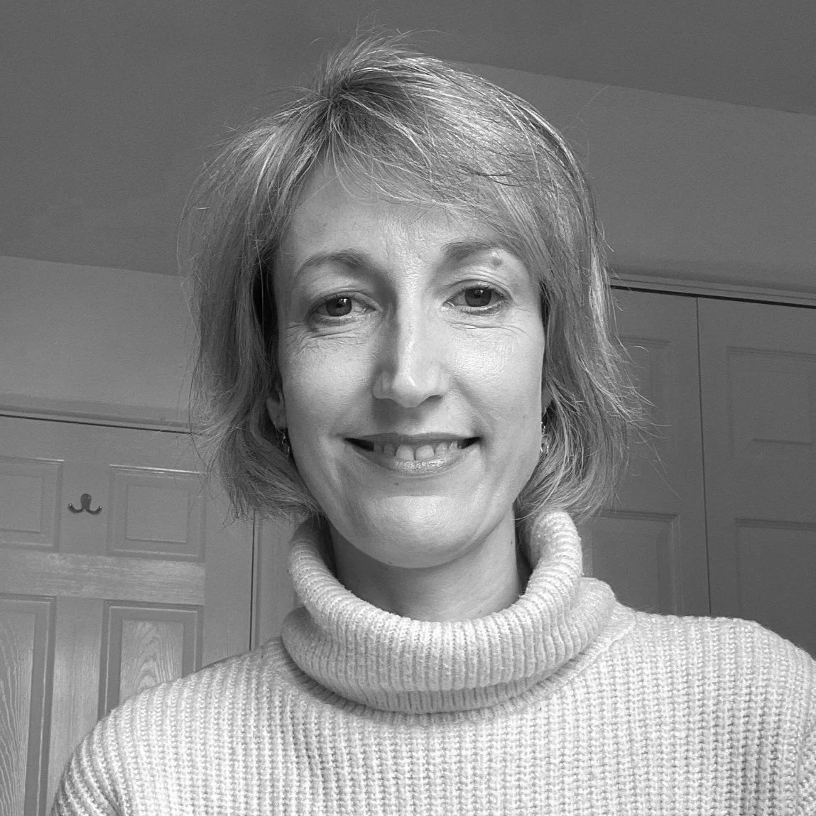 Black and white photo of a woman with short, wavy hair wearing a turtleneck sweater, smiling in an indoor setting.