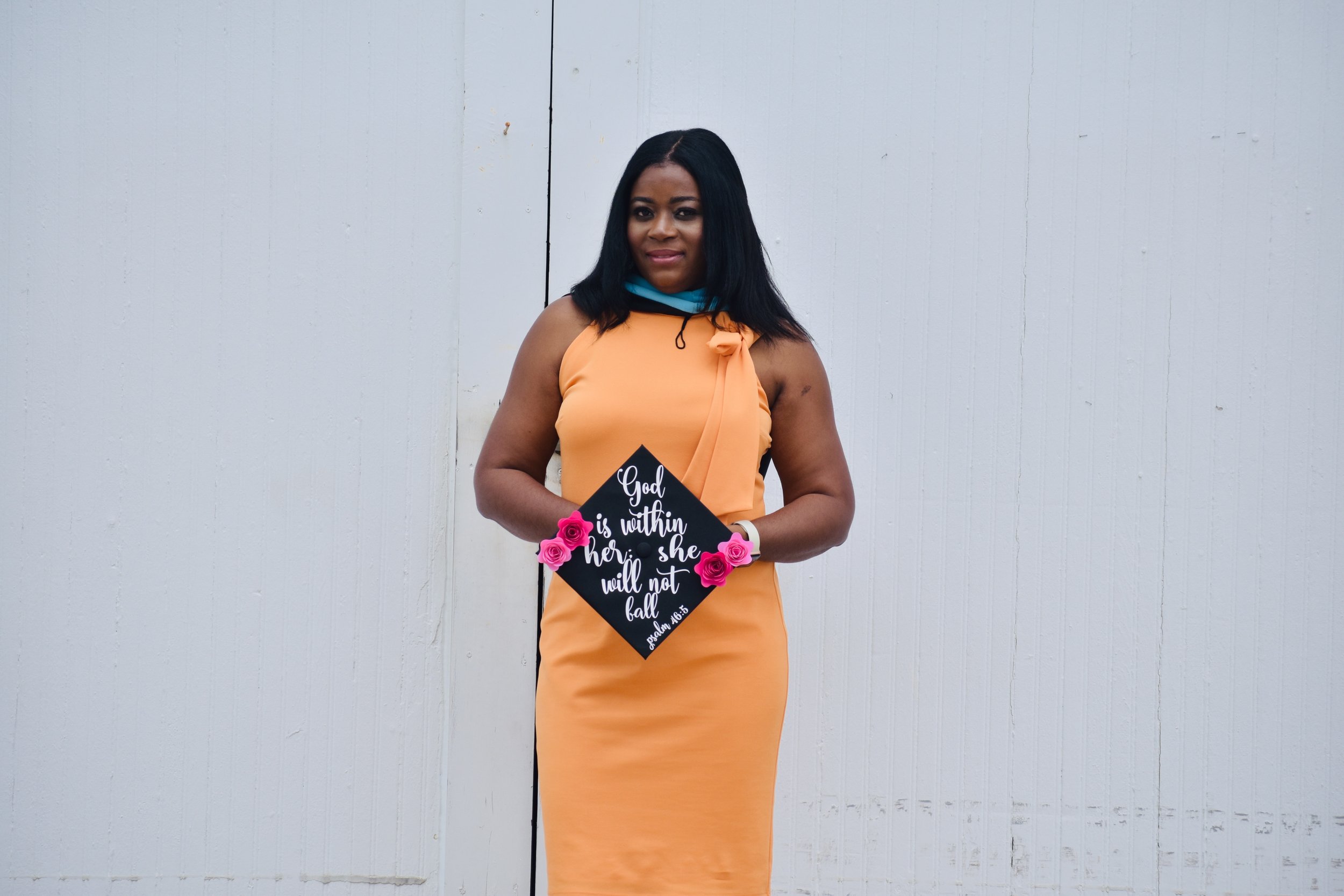 Woman in peach dress holding a sign with biblical quote, standing against a white wall.