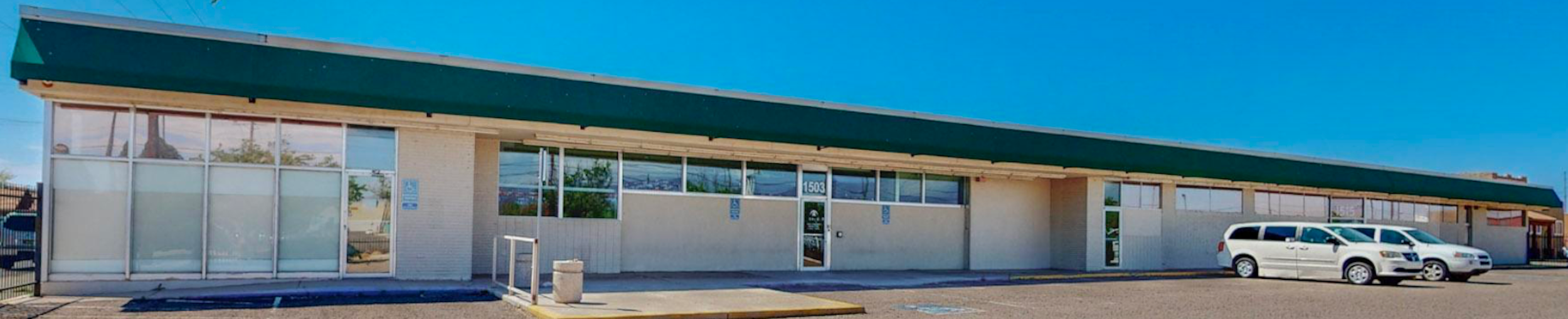 Exterior shot of the one story TGRCNM building with parked cars in front