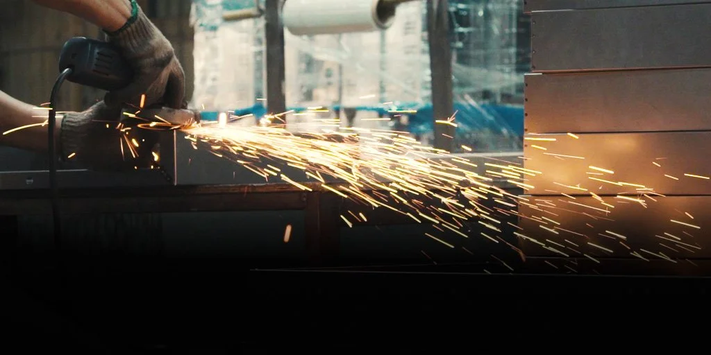 Person grinding metal with sparks flying, using an angle grinder, in an industrial setting.