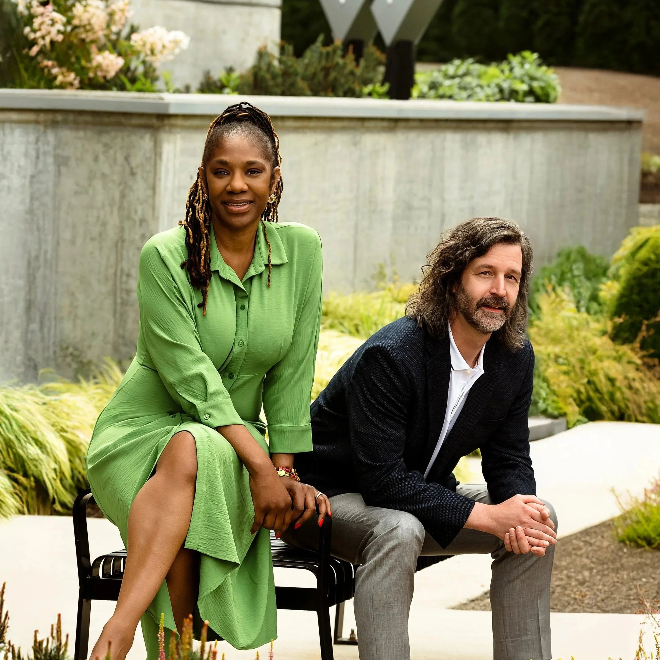 two real estate agents seated outdoors one african american female wearing green and one male with facial hair in sport coat