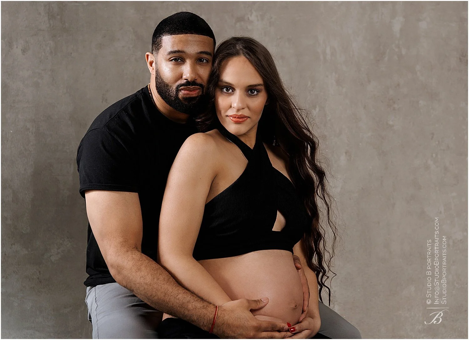 African American and Latina couple in studio posing together for their maternity photo shoot