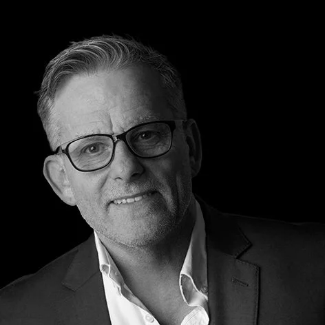 Black and white portrait of a middle-aged man wearing glasses and a suit, smiling slightly.