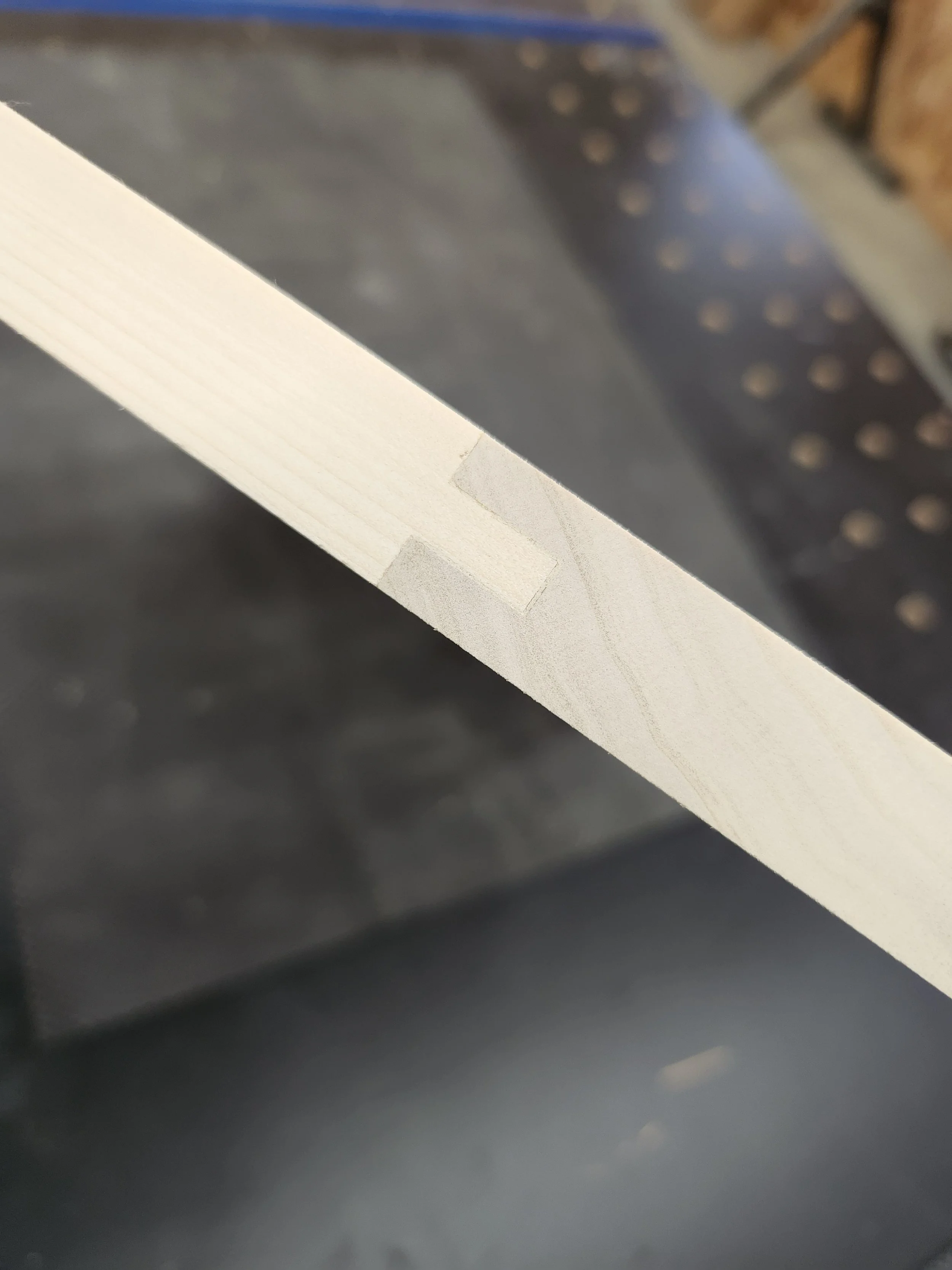 Close-up of a piece of light-colored wood with masking tape on it, likely in a workshop or carpentry setting.