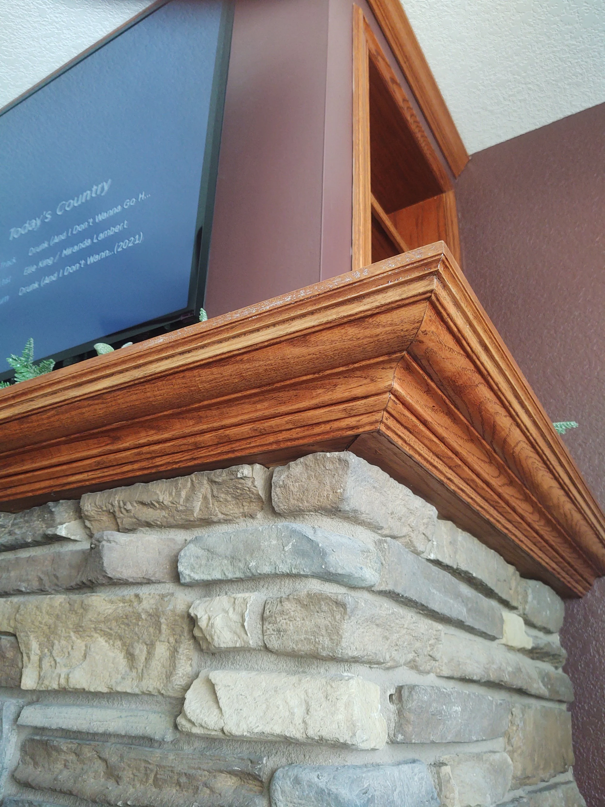 Close-up of a stone fireplace with a wooden mantel, with a flat-screen TV on top showing a blue screen with white text.