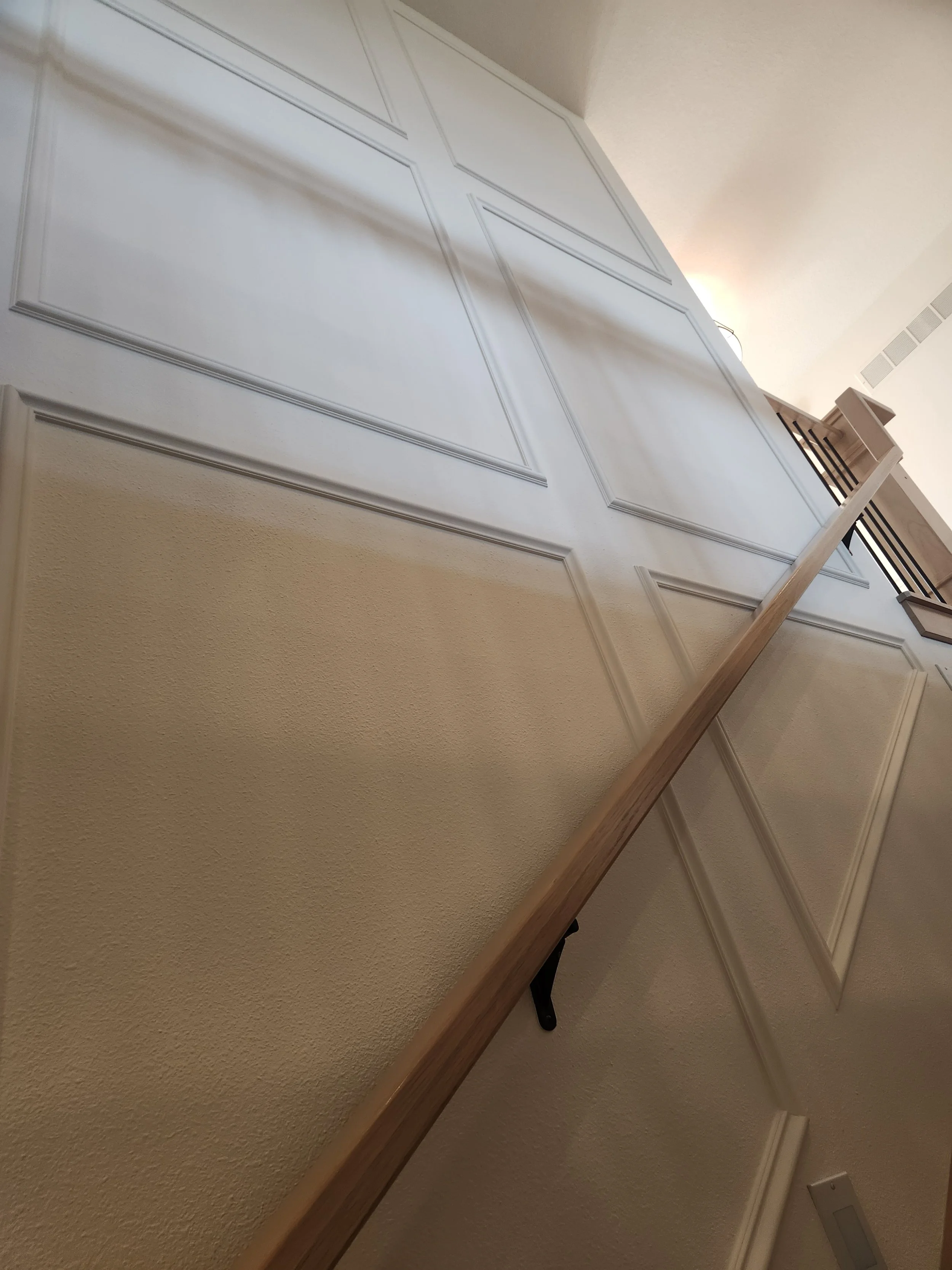 Interior view of a staircase with a wooden handrail and paneled wall.