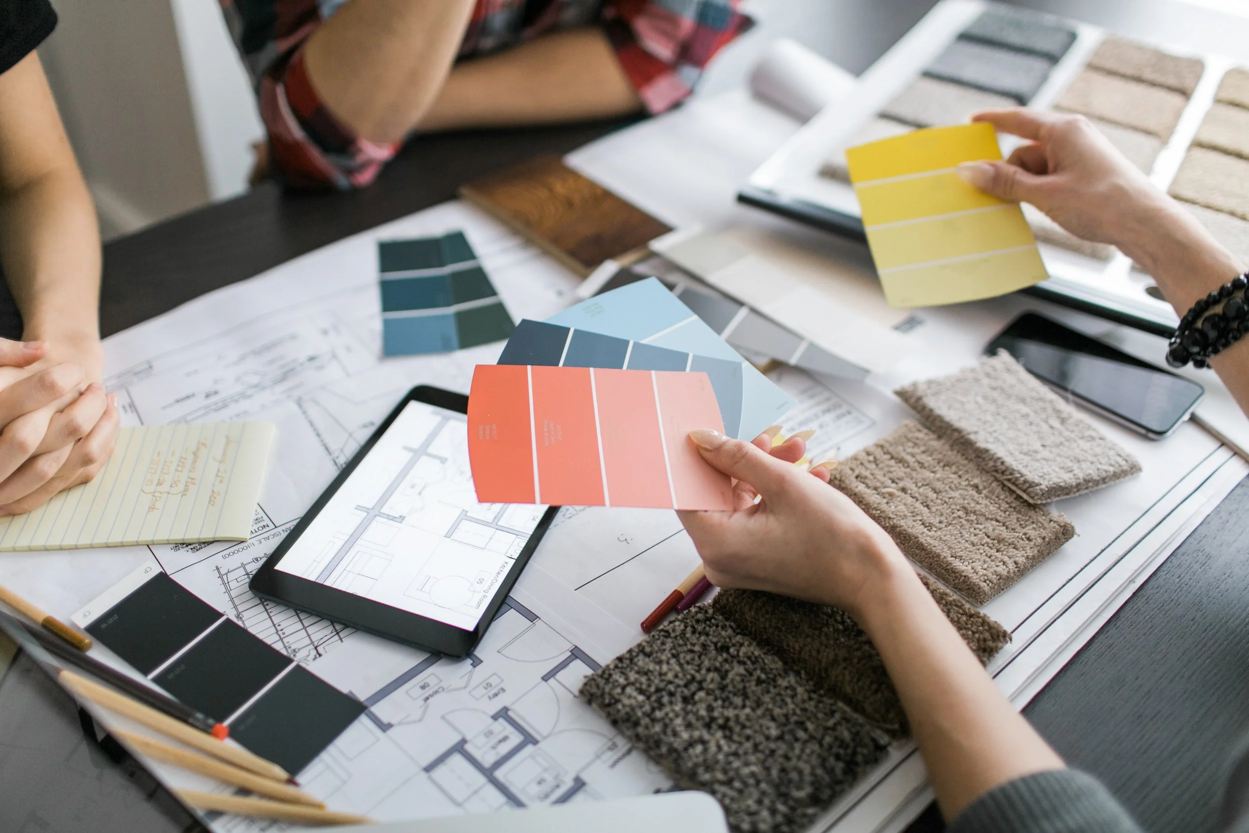 Two people working on interior design with color swatches, fabric samples, and floor plans on a table.