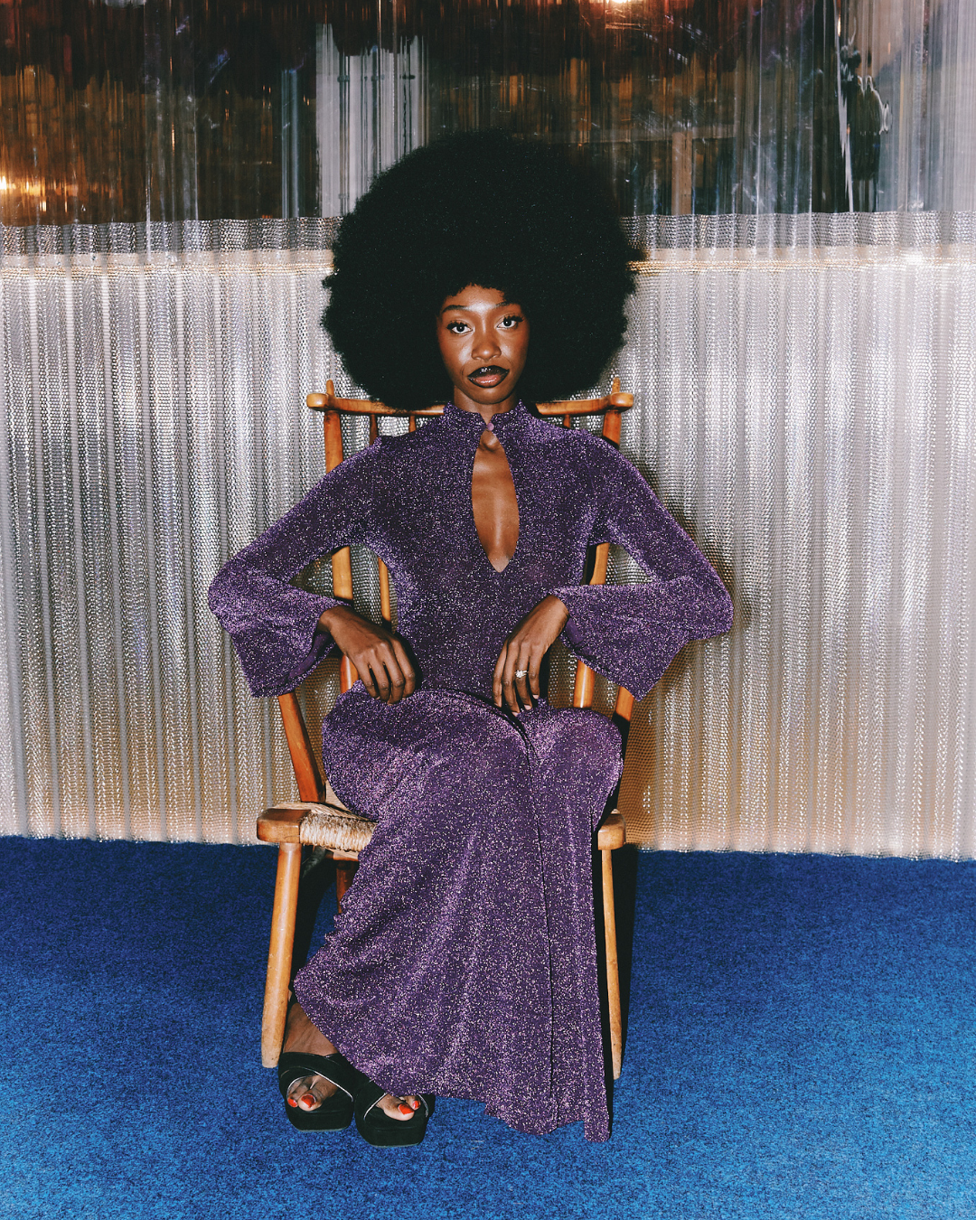 Poet Chloe Carterr hosting her event Rediscover You in London, wearing a purple sequin dress, sitting on a wooden chair.