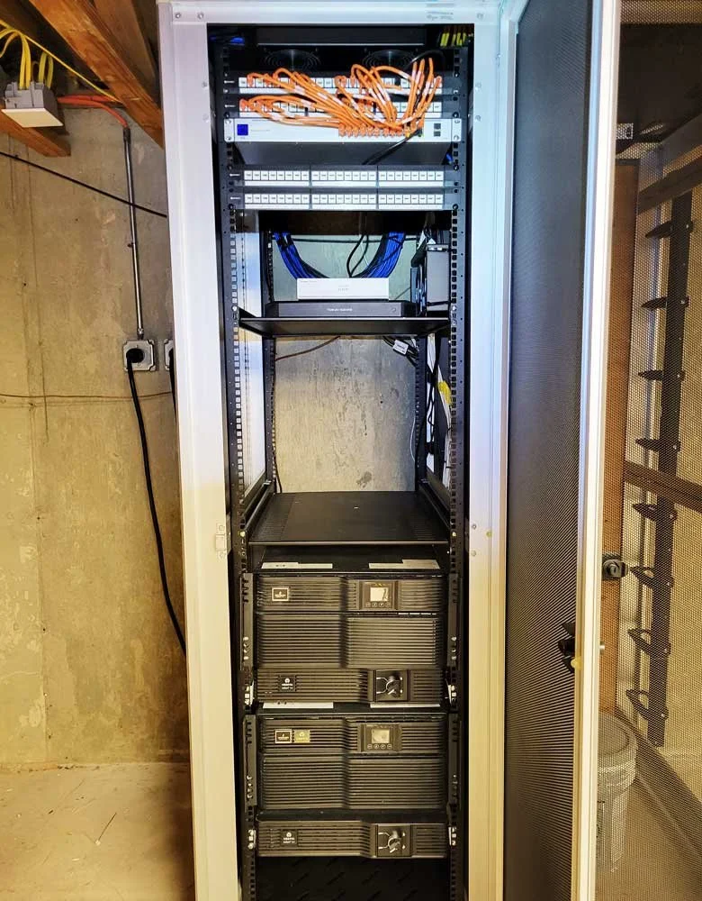 A server rack with networking equipment and power supplies, including orange network cables at the top and blue cables connected to devices at the middle.