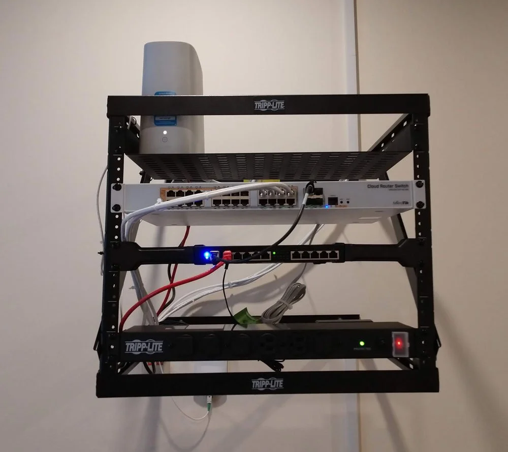 Server rack with networking equipment and power strips mounted on a wall.