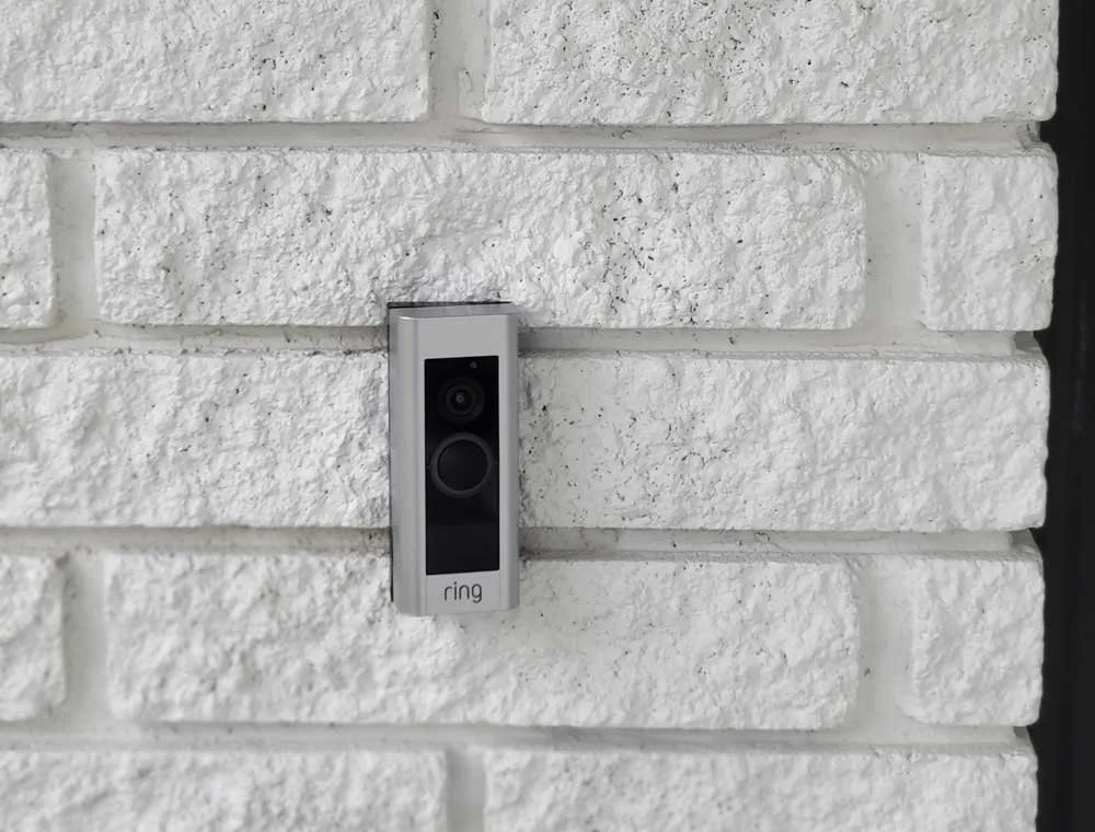 A Ring video doorbell mounted on a white brick wall.