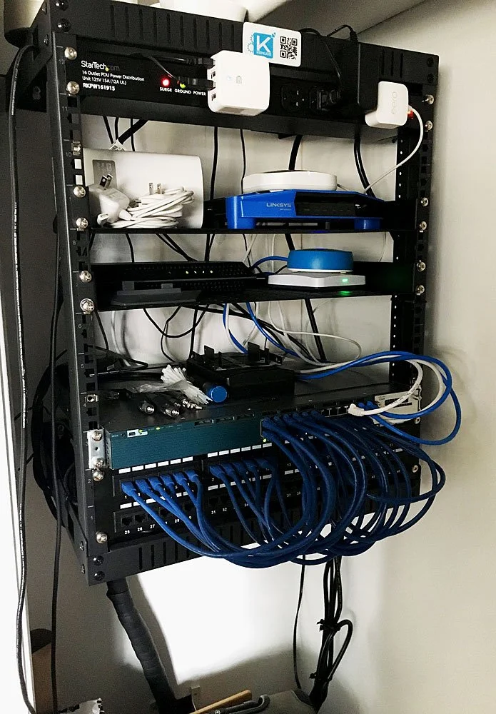 A black wall-mounted network equipment rack containing various electronic devices and cables.