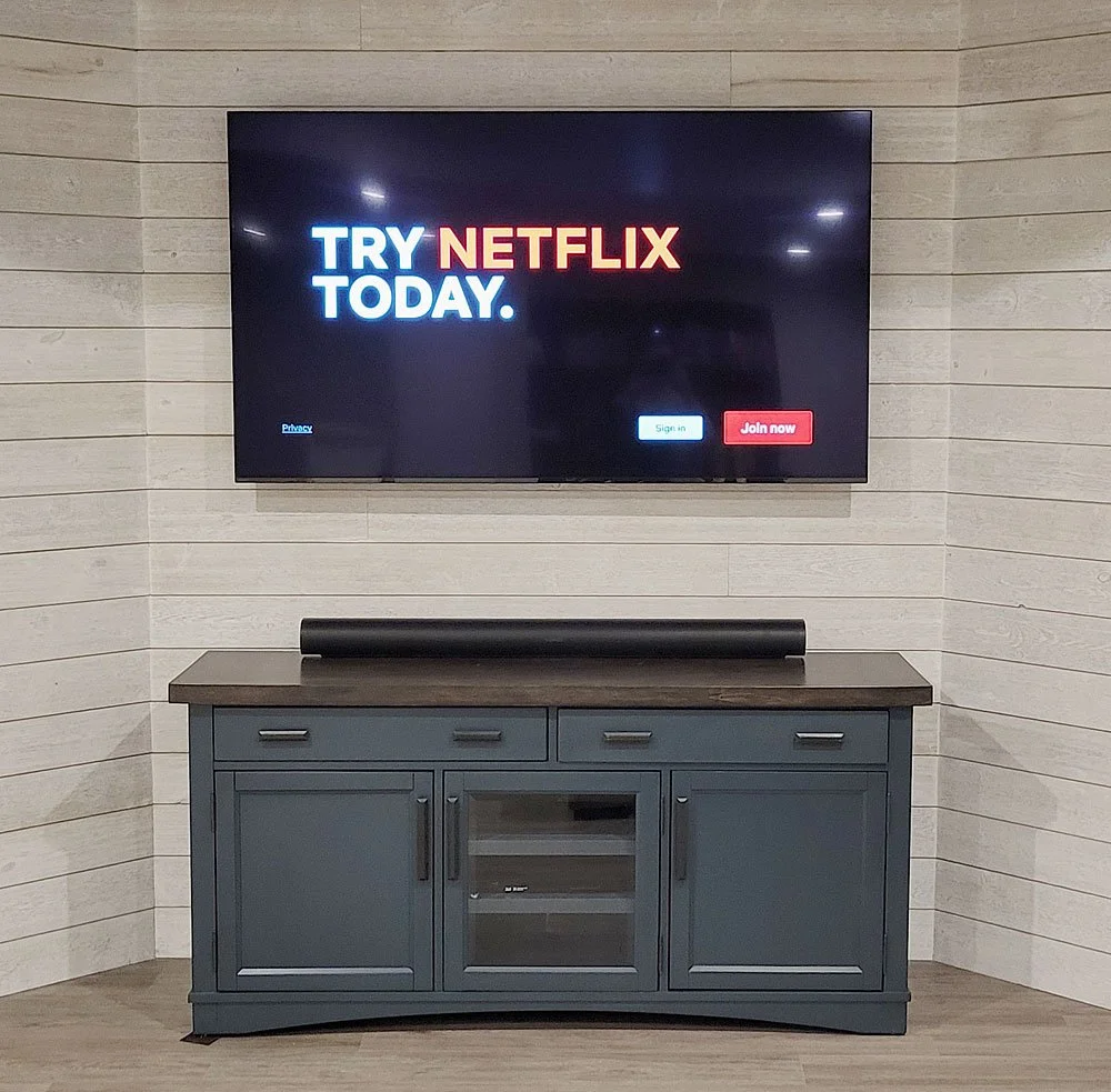 A television mounted on a wooden wall displays a Netflix promotion, with options to sign in or join now, above a blue cabinet.