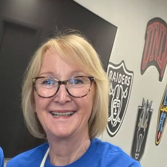 A woman with blonde hair and glasses smiling in a room with animated posters on the wall.