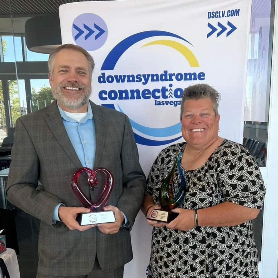 2024 Award honorees Jeramy Woods and Jennifer Winder smiling and posing 'Down's Syndrome Connection Las Vegas,' each holding a glass trophy.