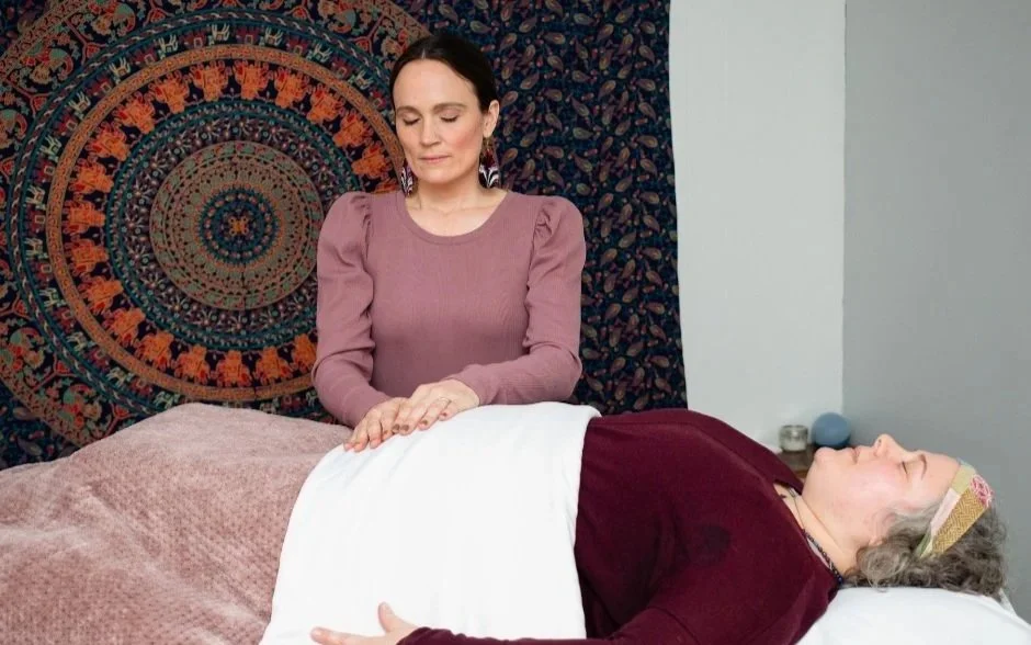 A woman receiving a massage from a massage therapist in a peaceful setting with a colorful mandala wall hanging.