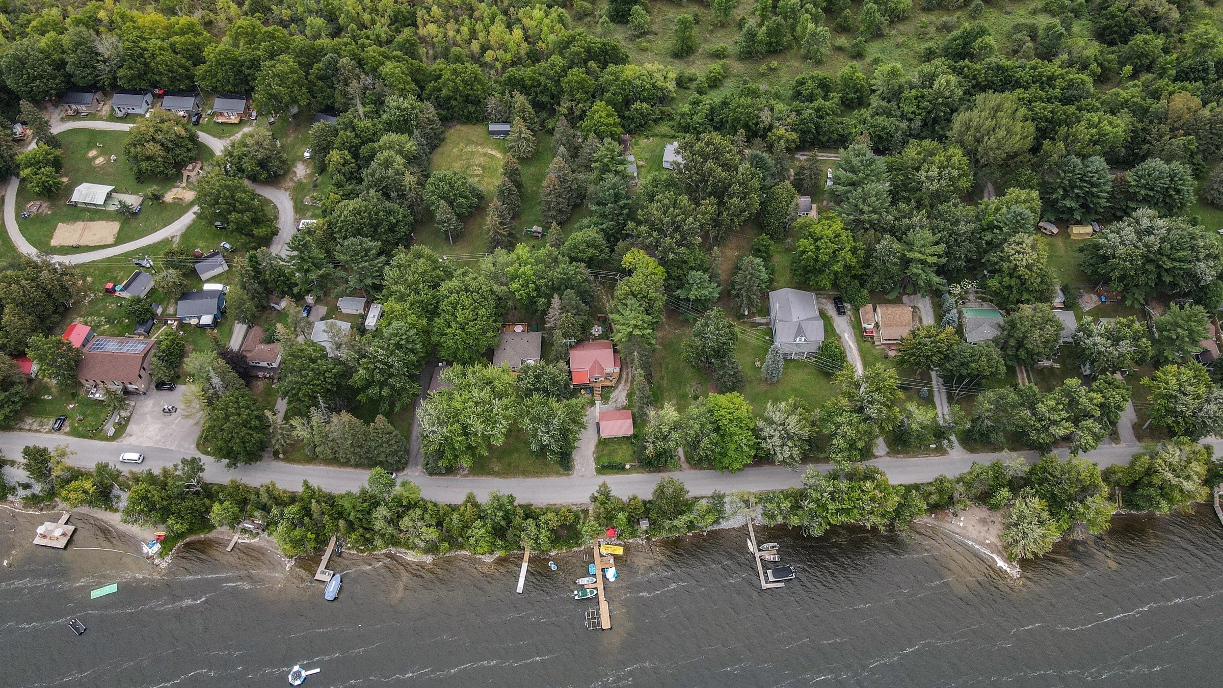 Aerial view of cottages set back from the water behind a shoreline road at Lake Dalrymple, with private docks along the water's edge, Ontario