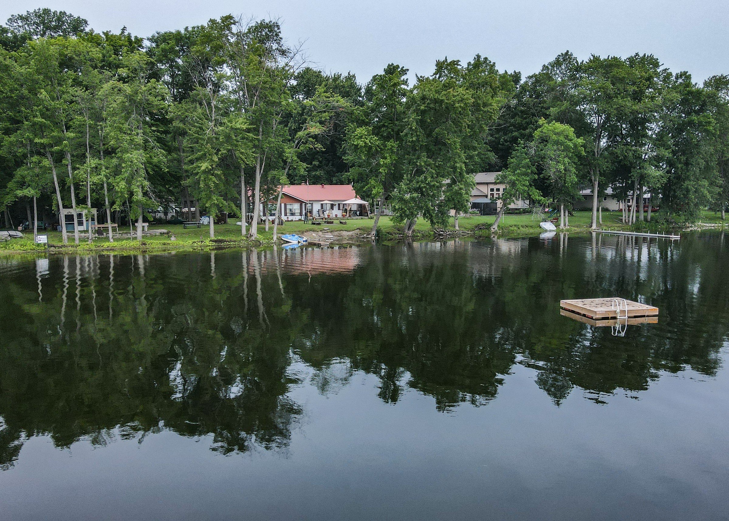 Swim raft floating on the calm water of Lake Dalrymple with a treed cottage shoreline reflected behind it, Kawartha Lakes, Ontario