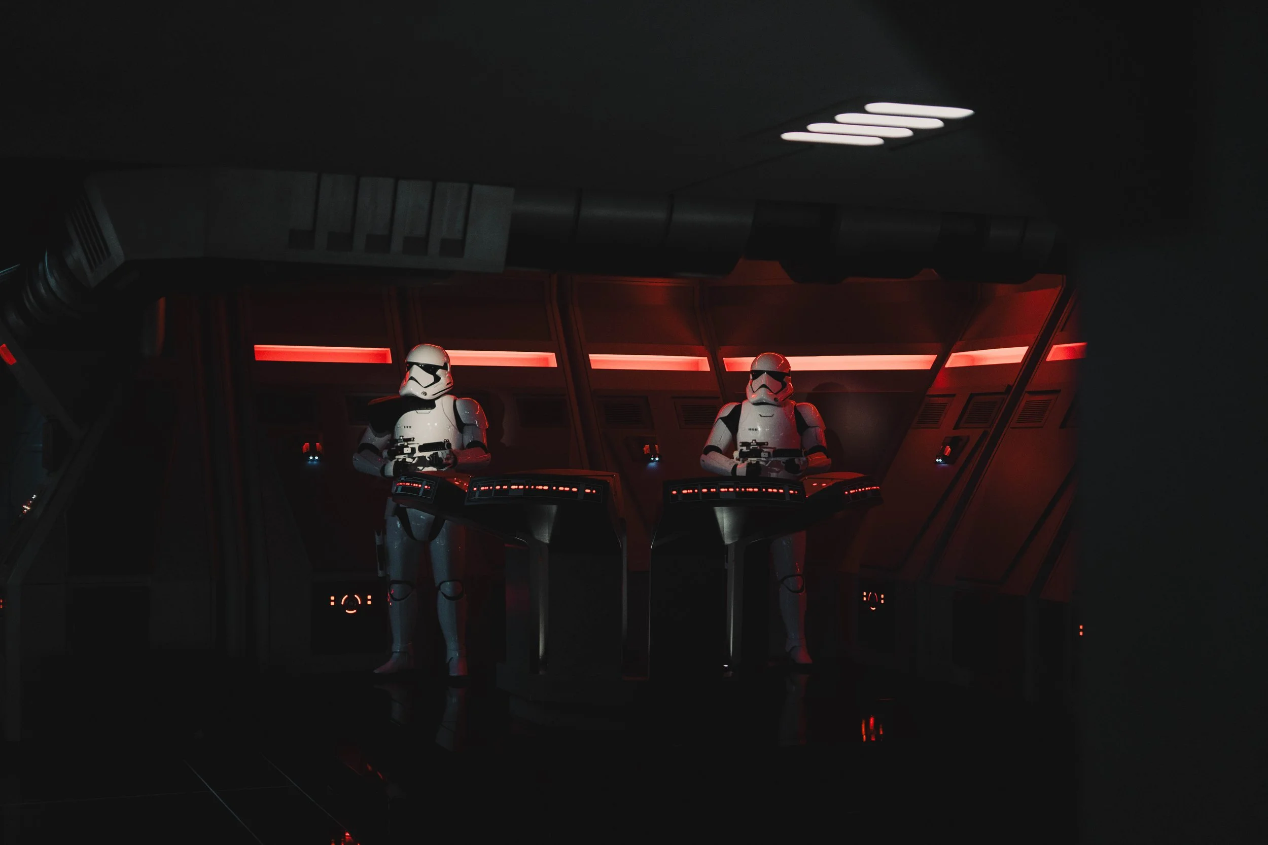 Two stormtroopers inside a spaceship control room with red lighting, standing at control panels.
