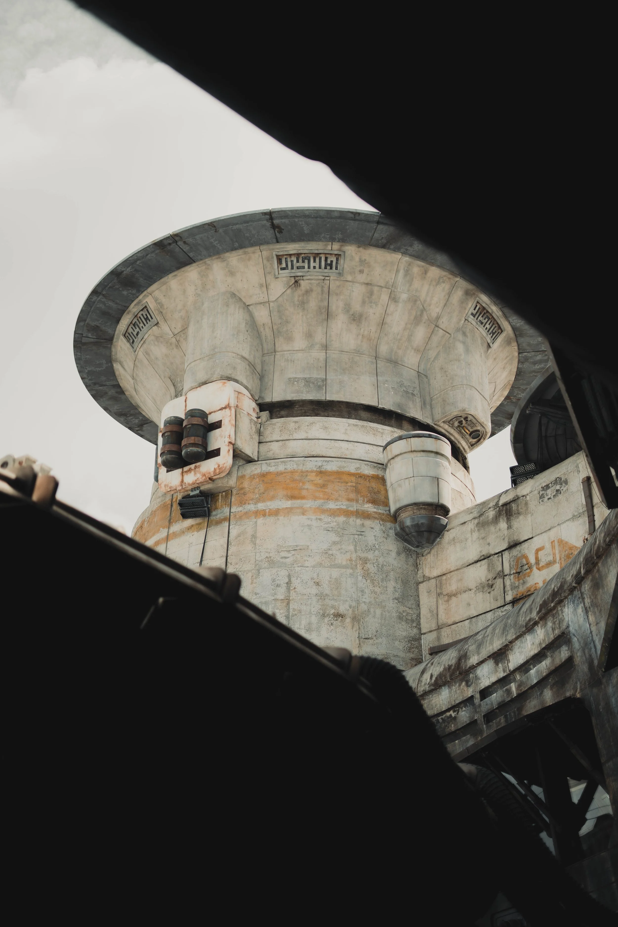 A large, circular industrial structure or tower viewed from below, framed by dark foreground elements.