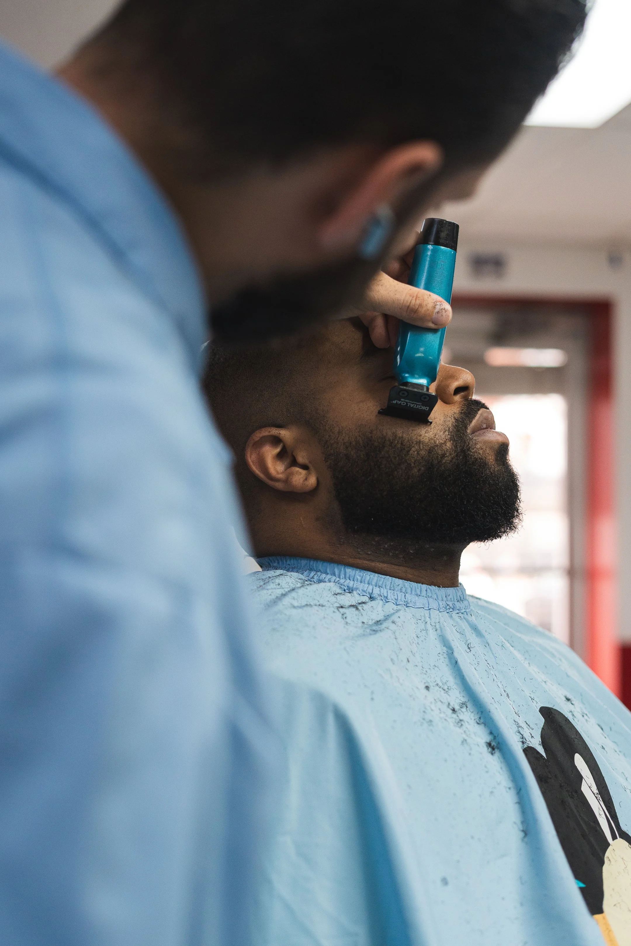 Barber shaving a man's beard with a straight razor in a barbershop.
