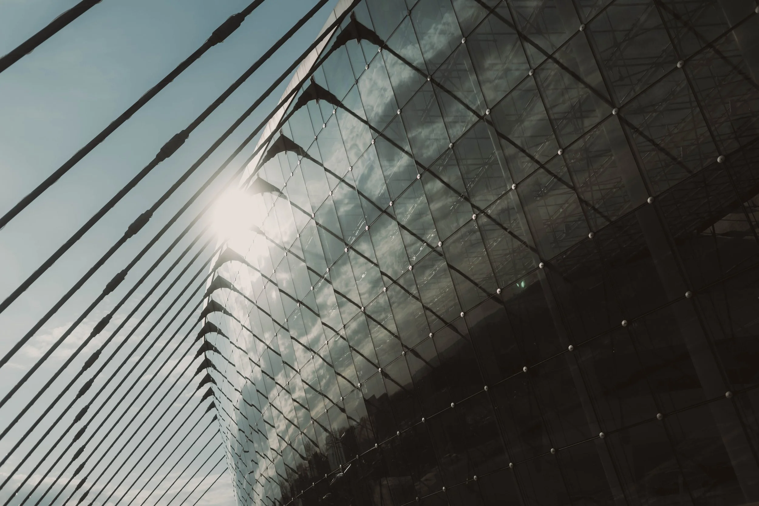 Modern glass building with reflective windows and a sun glare in the sky.