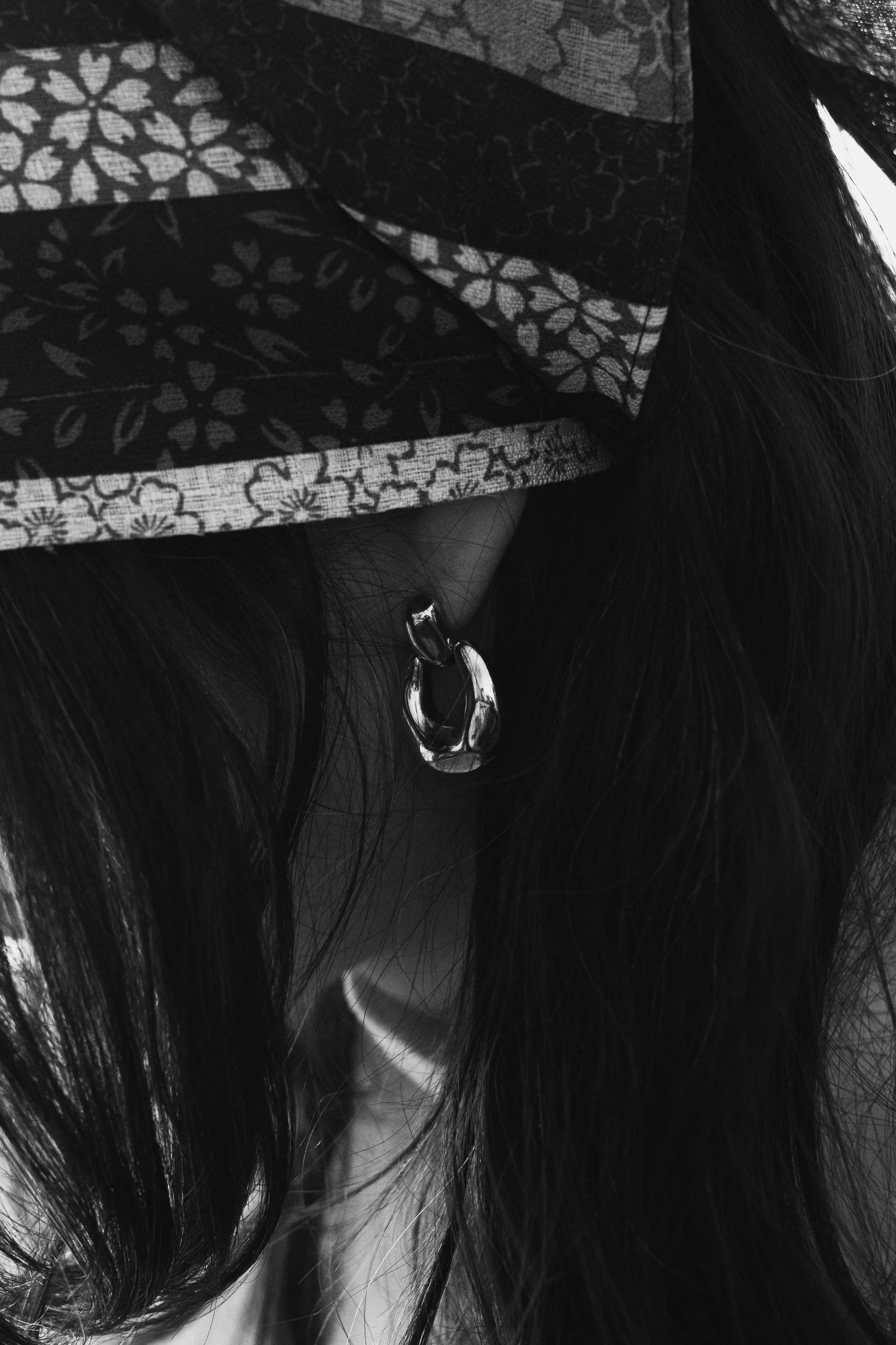 Close-up of a person wearing a patterned headscarf and silver hoop earrings, with long dark hair.