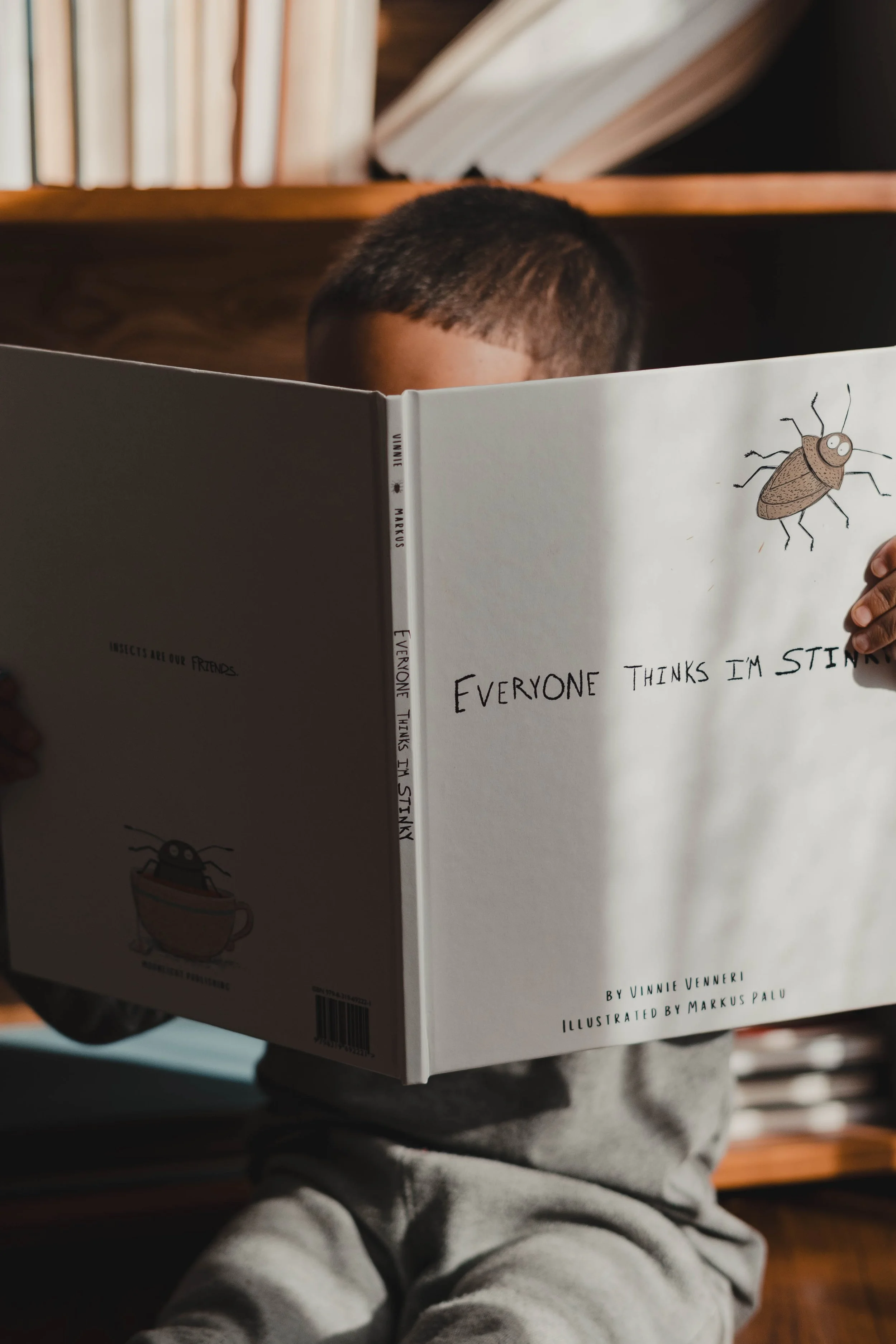 Child sitting and reading a book titled 'Everyone Thinks I'm Stinky,' featuring cartoon illustrations of bugs on the cover, book on sale at Barnes & Noble.