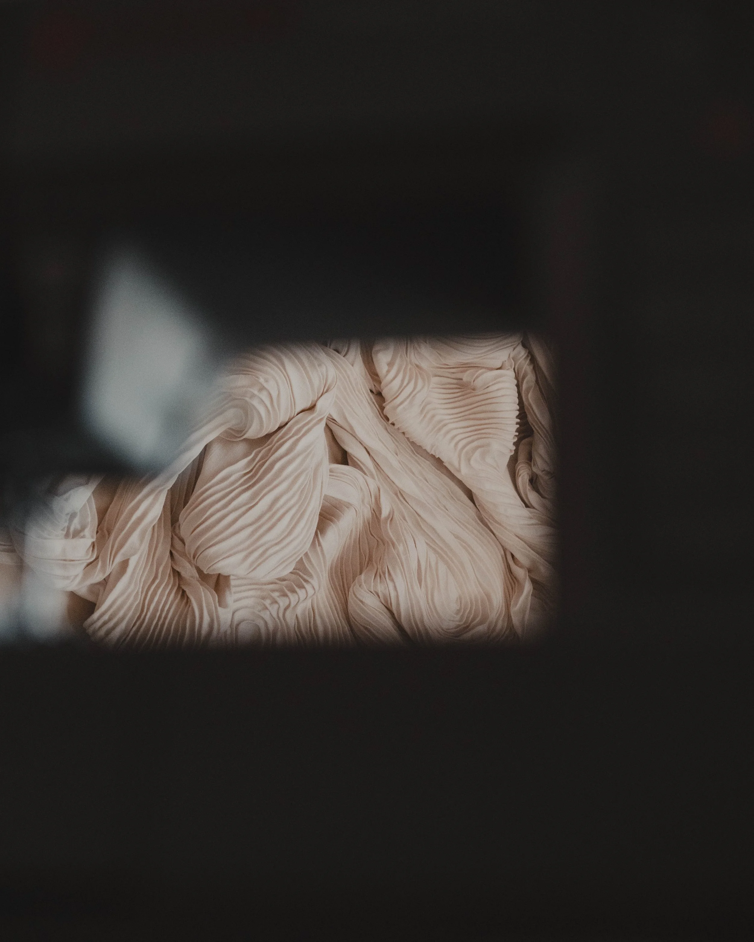 Cream-colored, pleated fabric viewed through a narrow opening or gap.