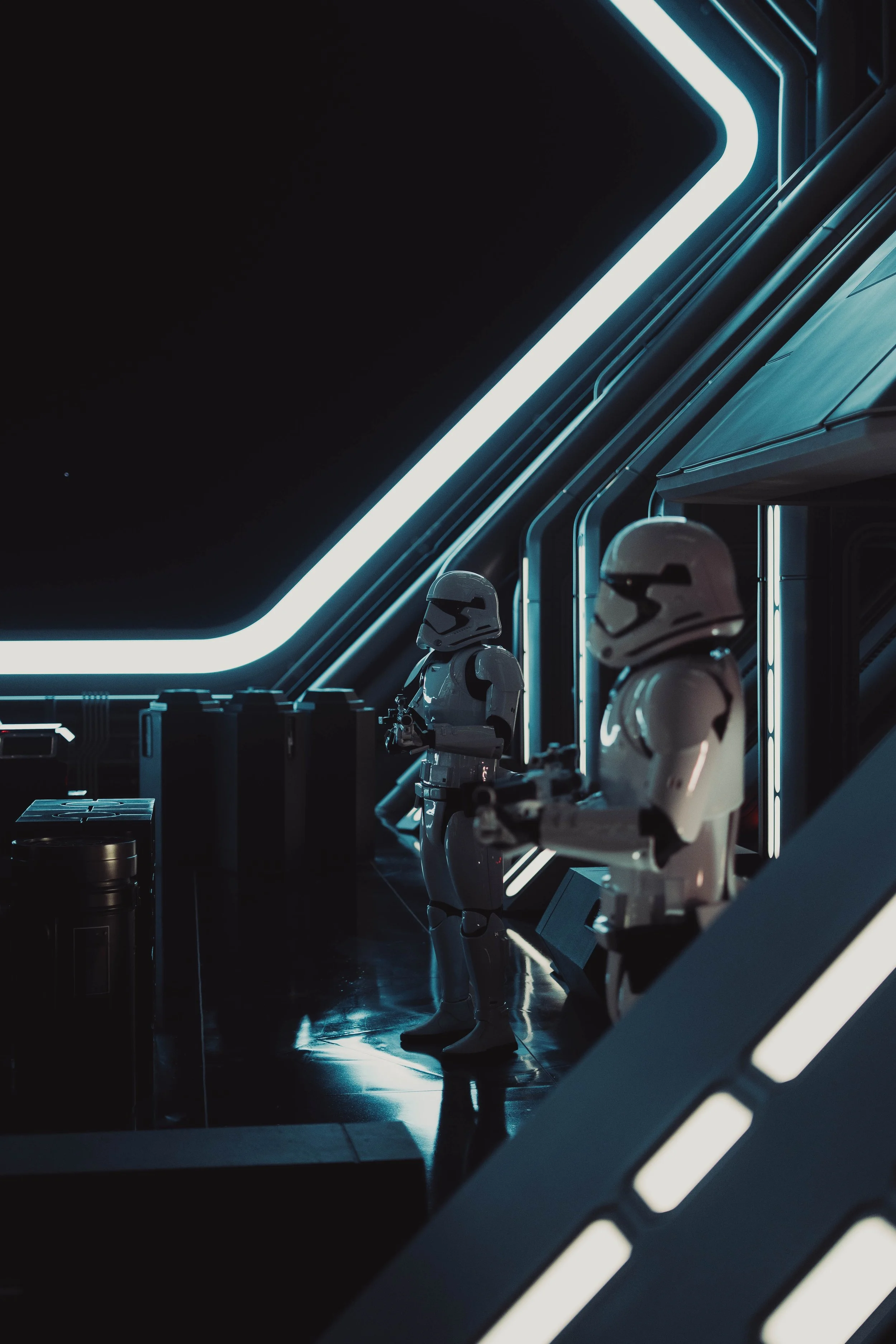 Two stormtroopers in a futuristic, dark sci-fi setting illuminated by neon blue lights.
