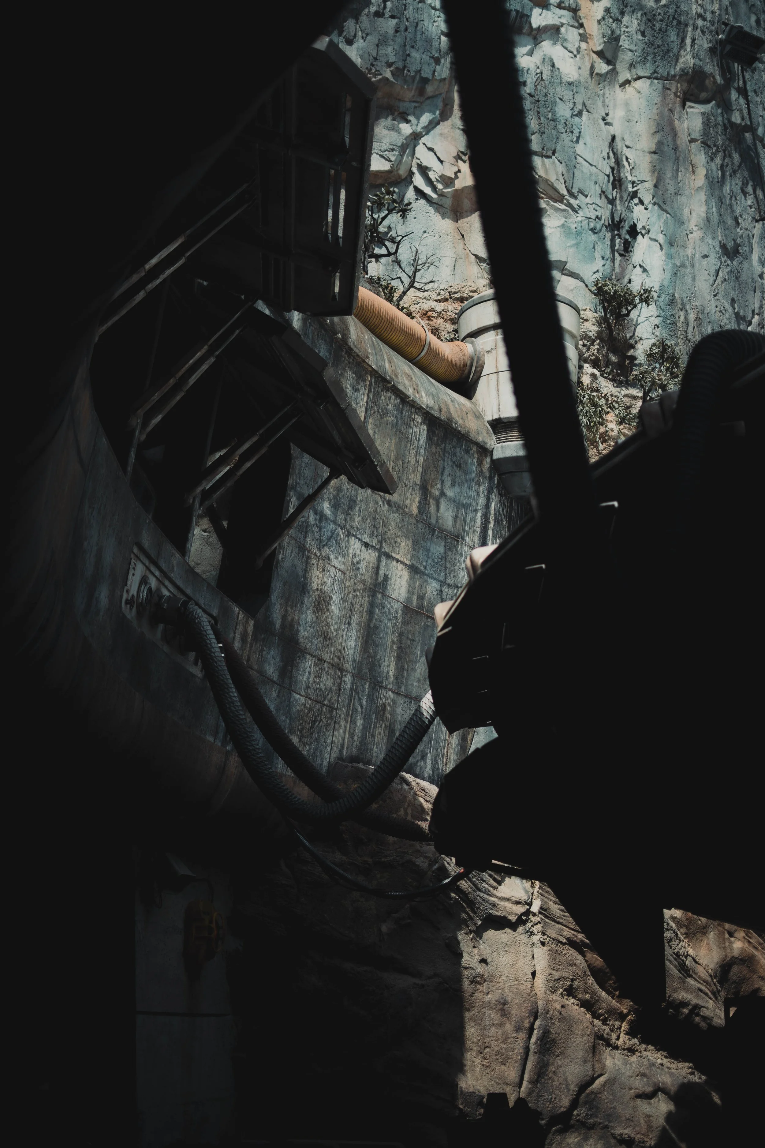 Close-up of mechanical equipment or machinery against a rocky background, with black framing and pipes or hoses connected to the equipment.