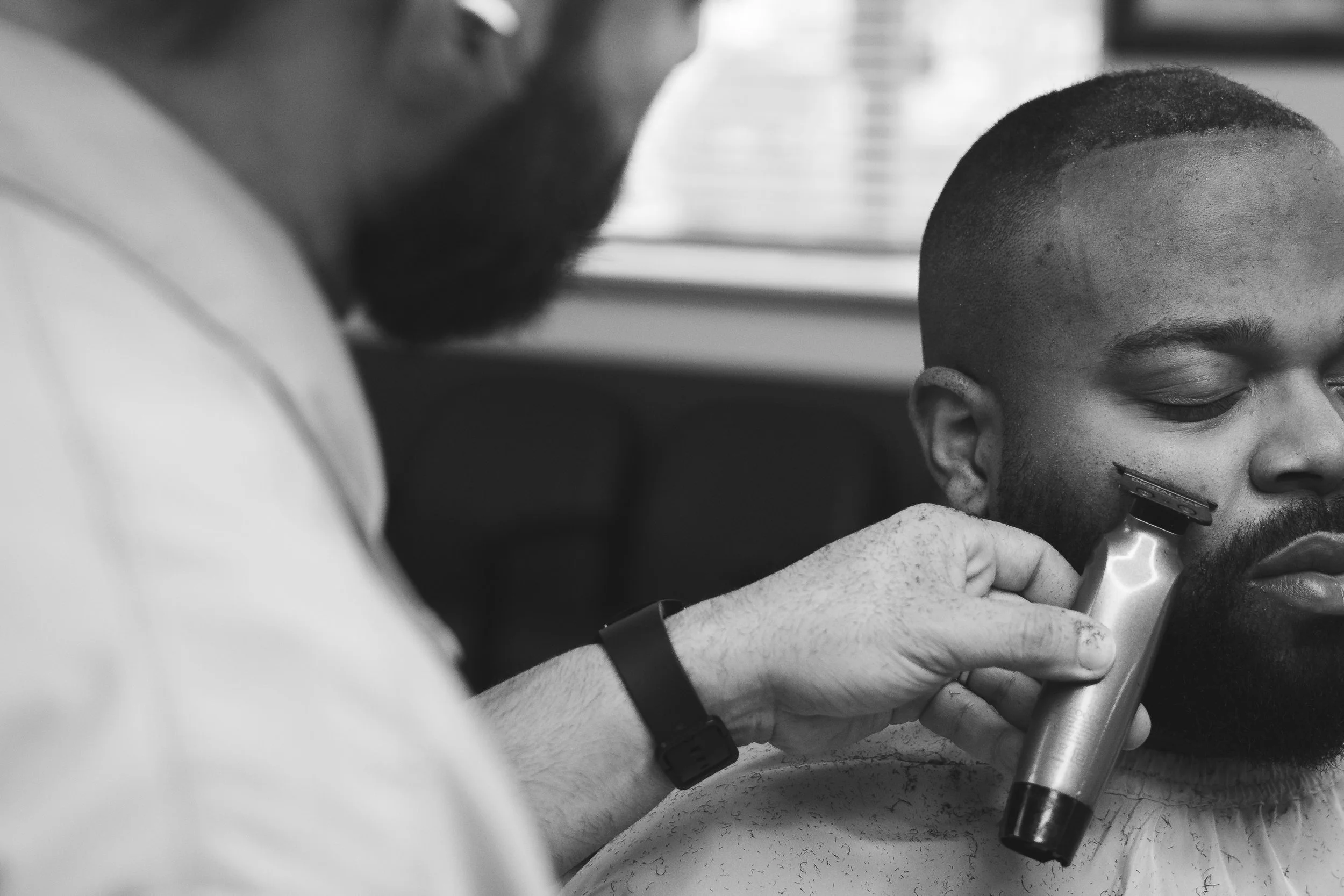 Barber using electric clipper to shave a man's beard in a barbershop.