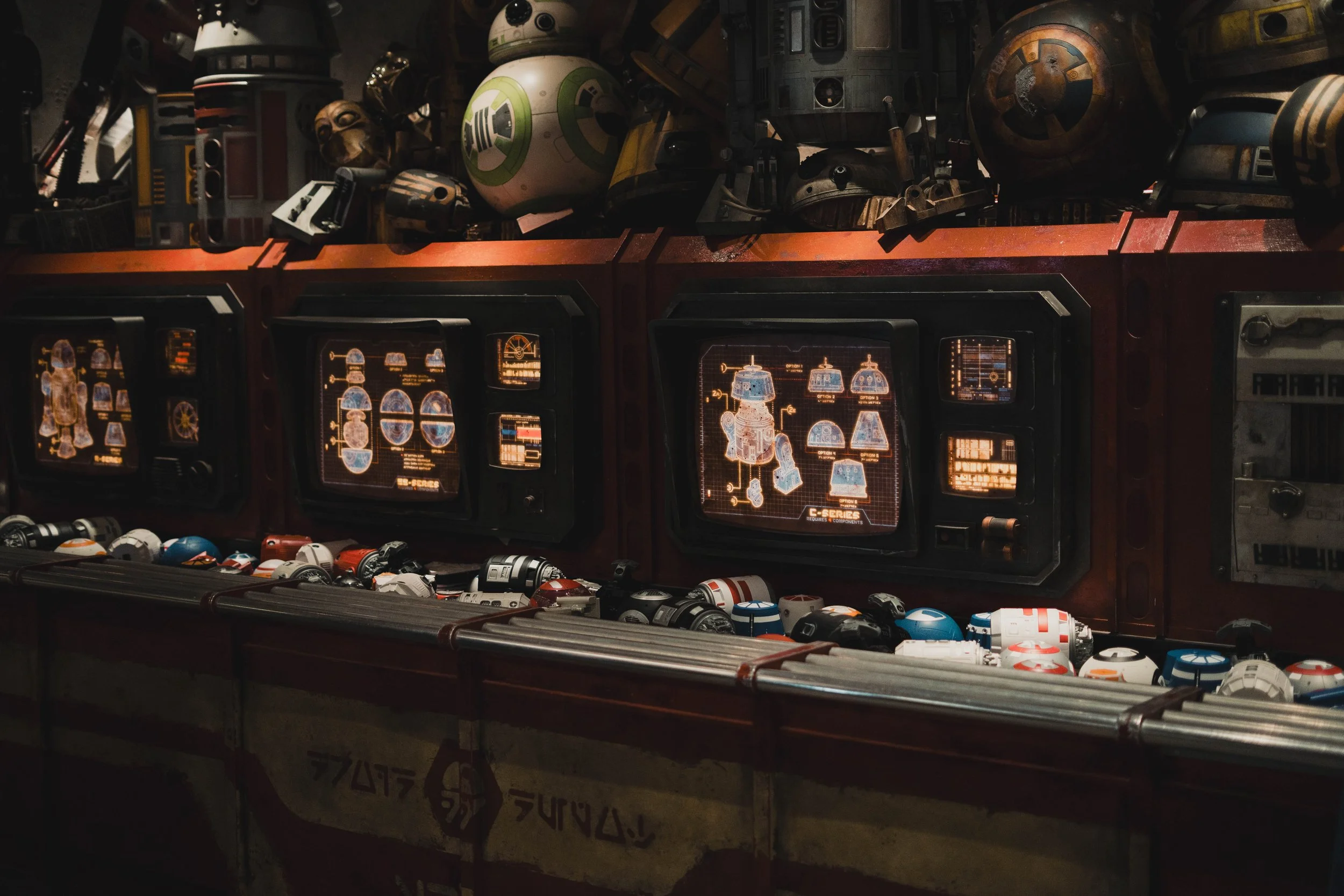 Display of toy Star Wars droid figures and helmets on a table with digital screens showing schematics of a robot, set in a sci-fi environment.