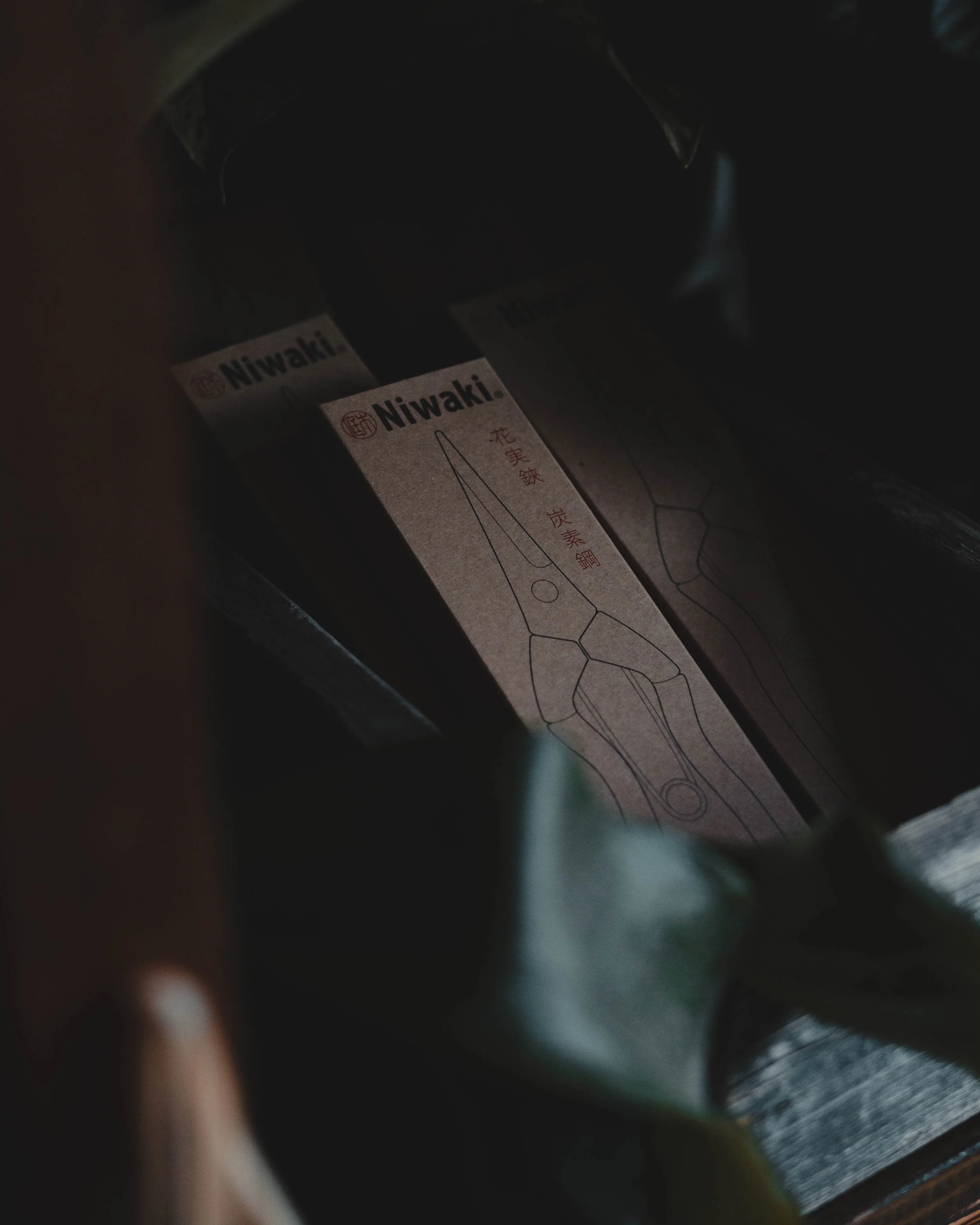 A partially visible hand holding a bag containing Niwaki pruning shears in a dark setting.
