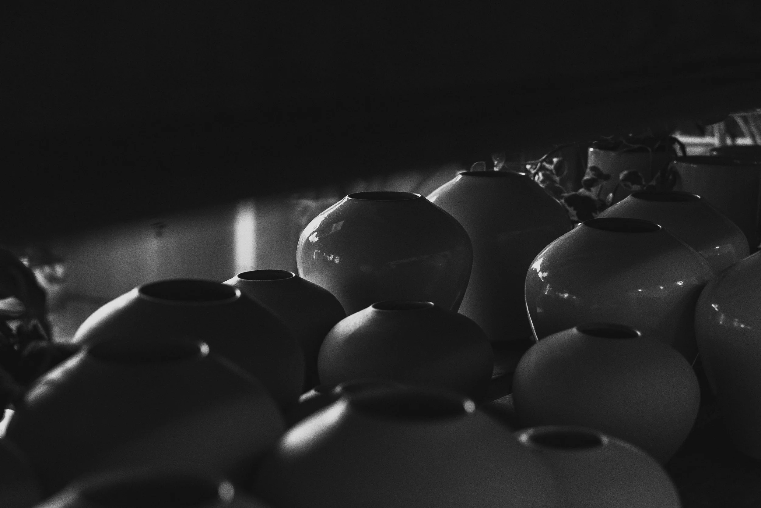 A collection of ceramic vases arranged on a surface, with some partially hidden, under a dark ceiling in a dimly lit room.