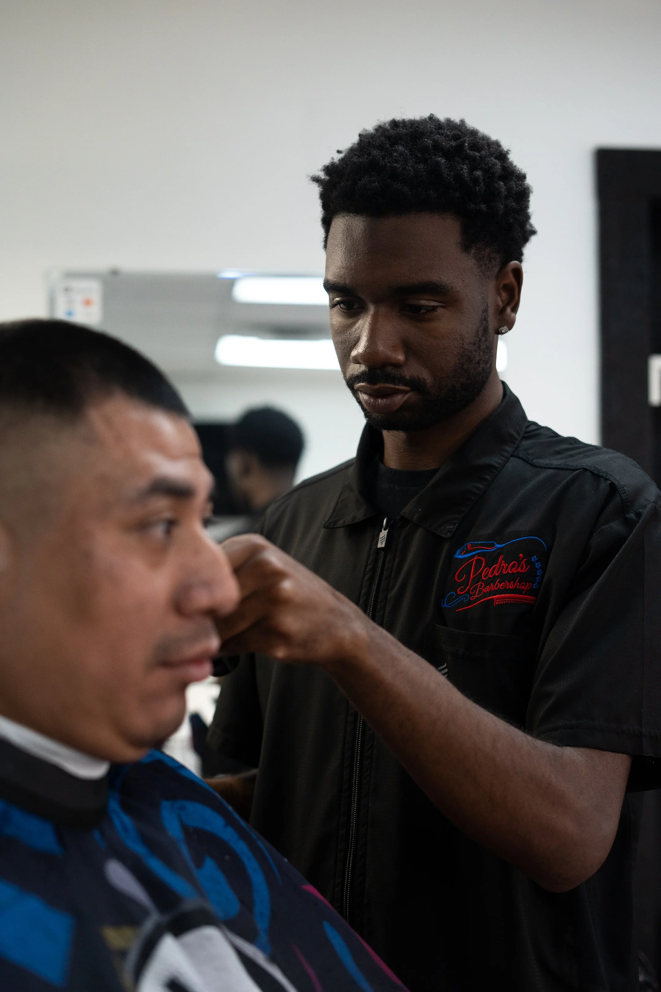 Barber trimming and styling a male client's hair in a barbershop.